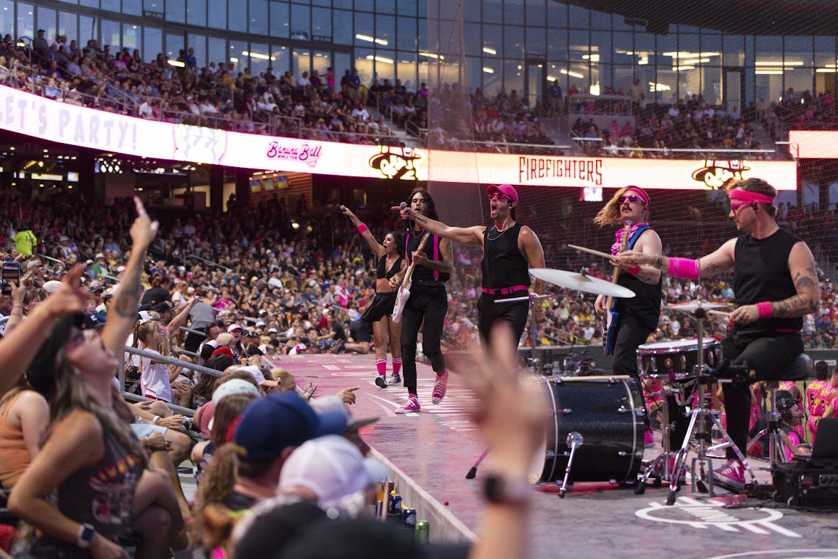 Crowd in stadium watching performers on stage with musical instruments and microphones.