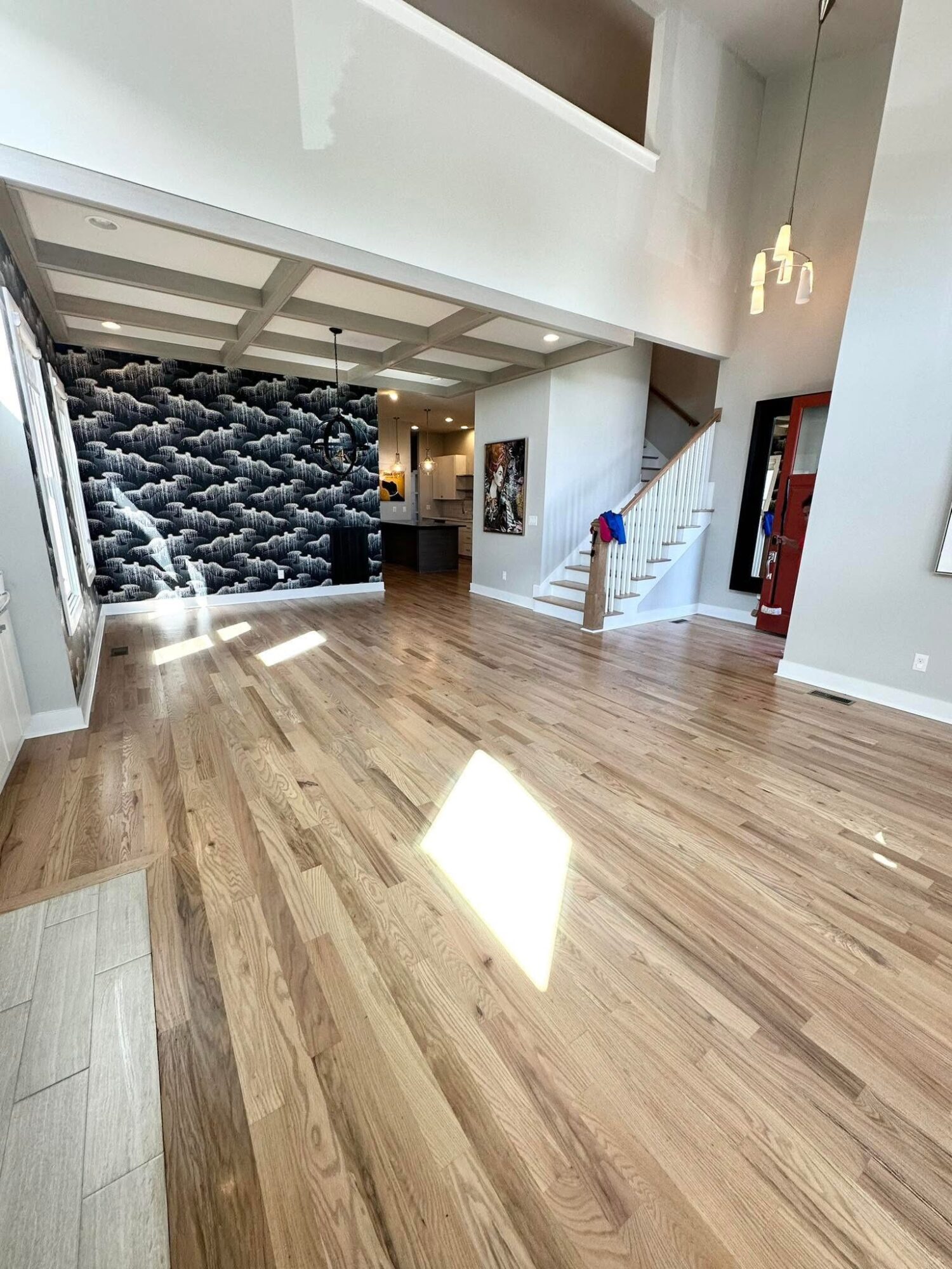 Spacious living area with wooden floor, staircase, and textured wall feature, illuminated by natural light.