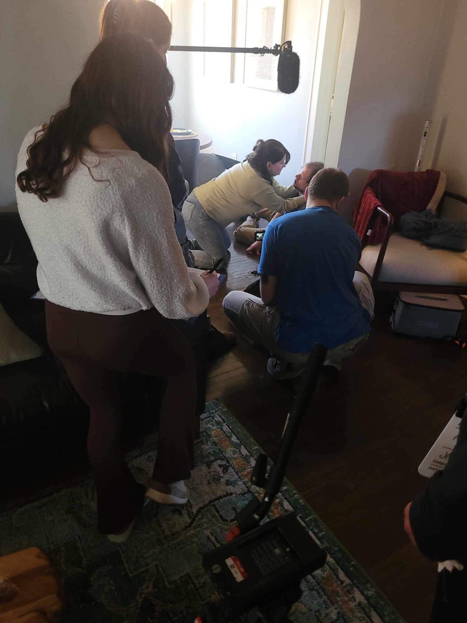 People gathered in a room, some sitting and some standing, with a camera or equipment on the floor.