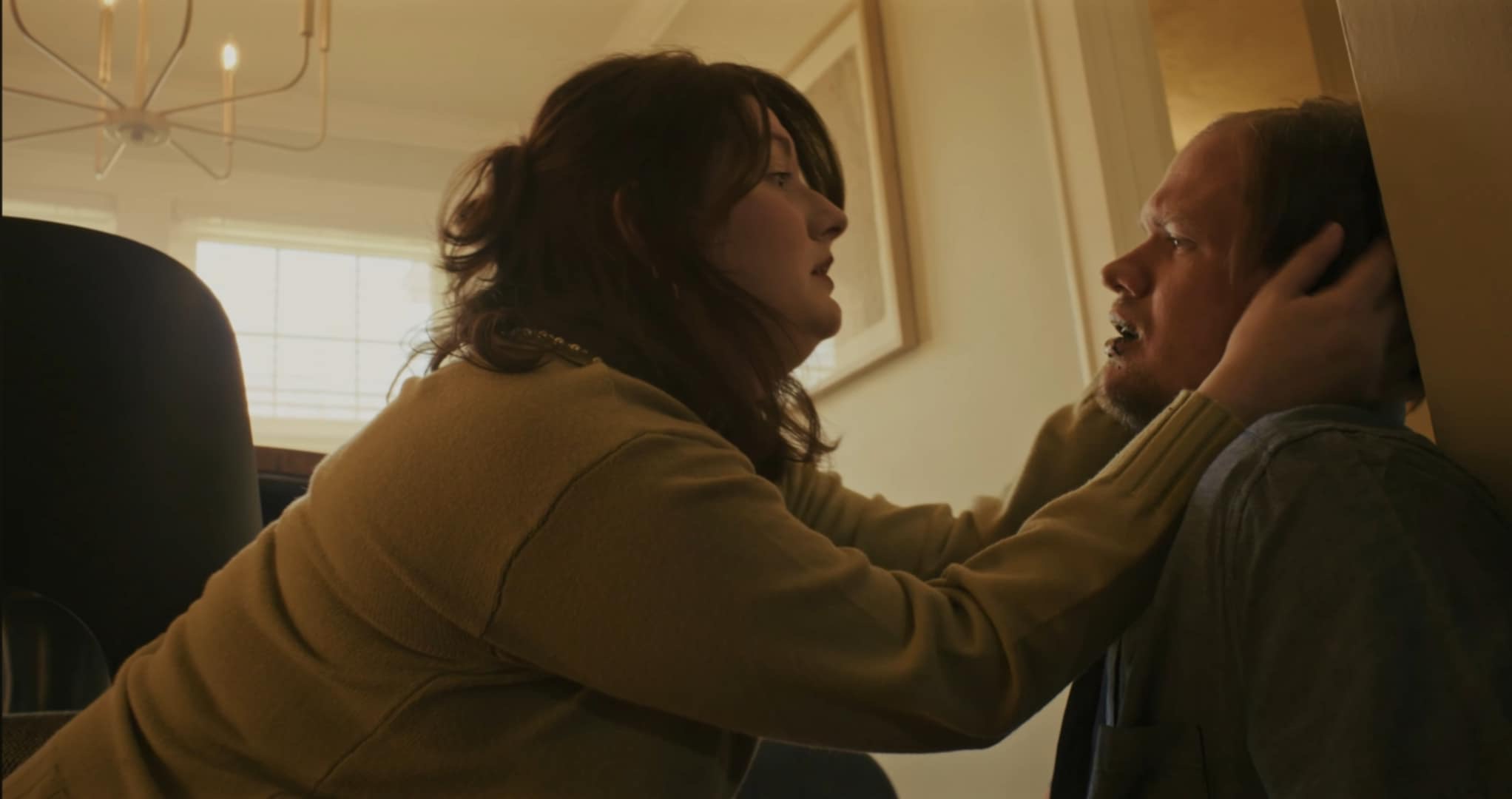 Woman gently touches man's face indoors with window and framed picture behind them.