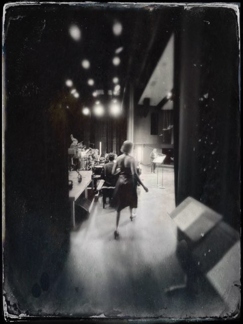 Person walking through a dimly lit indoor space with musical instruments and stage equipment.