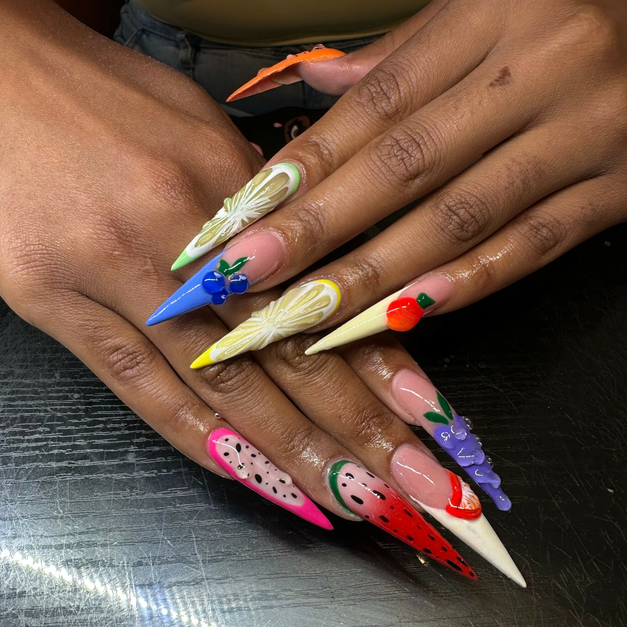 Hands with colorful, decorated long nails resting on a black surface.