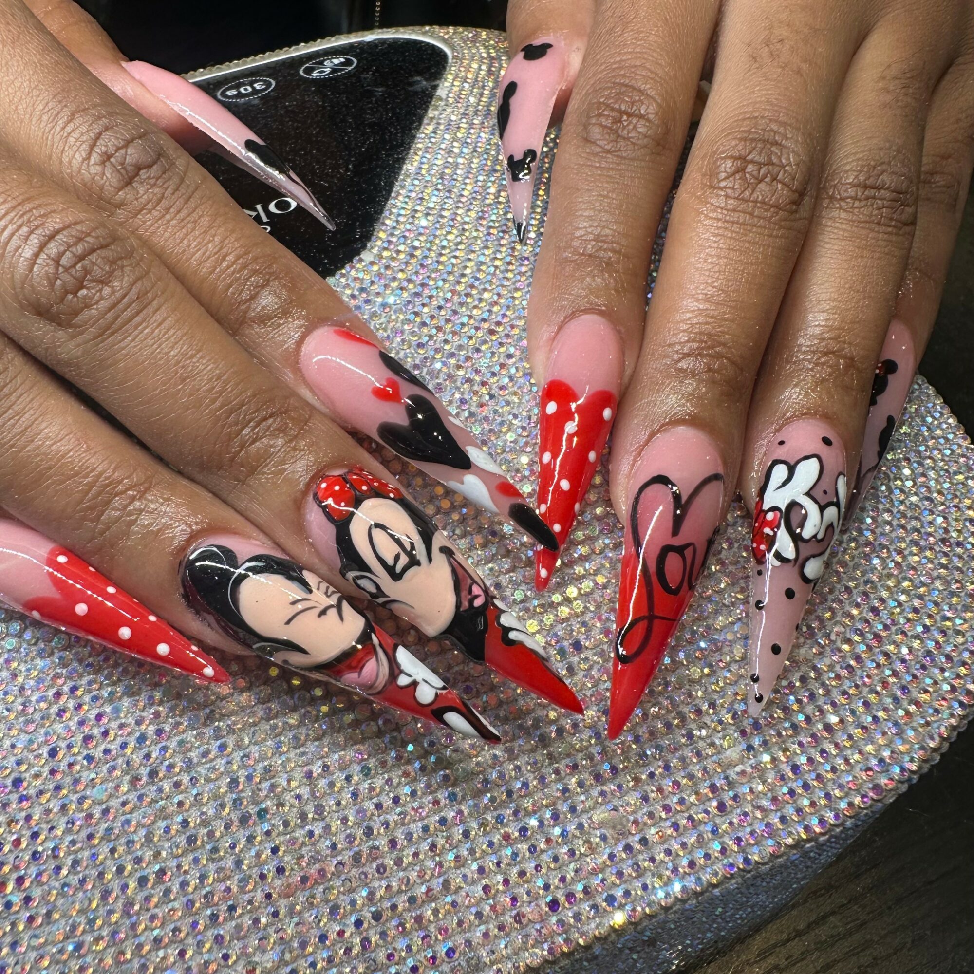 Hands with colorful, decorated nails resting on a glittery surface, showing various nail art designs.