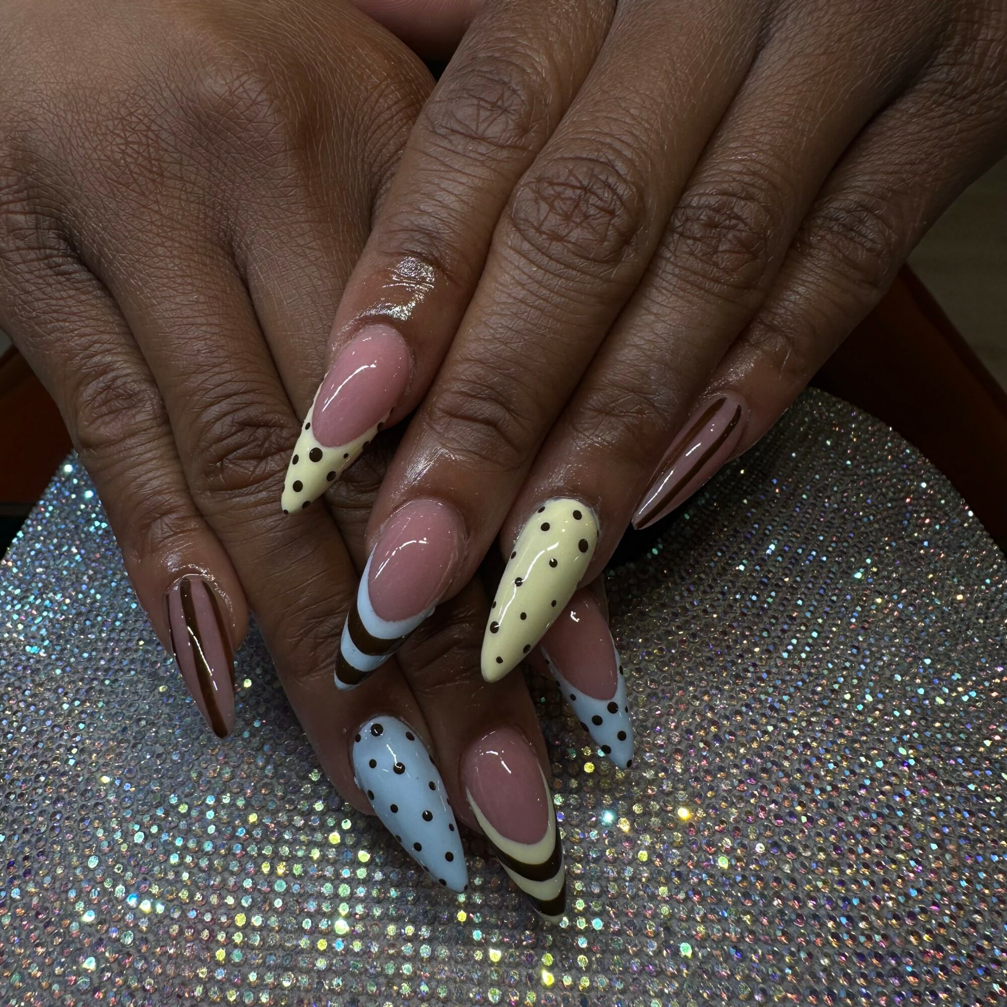 Close-up of hands with decorated nails resting on a glittery surface.
