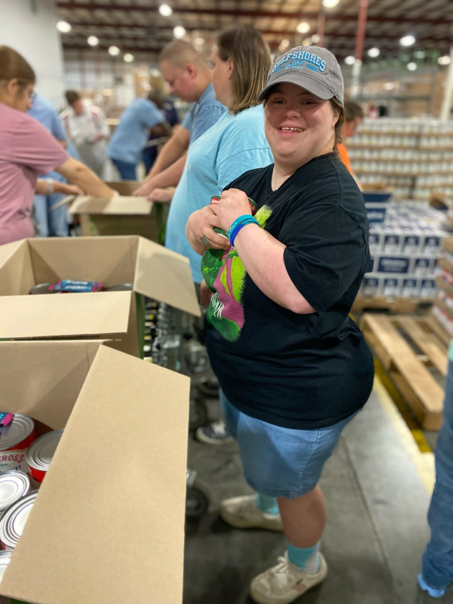 Smiling girl wearing a cap and black shirt, standing in a warehouse with boxes and other children.