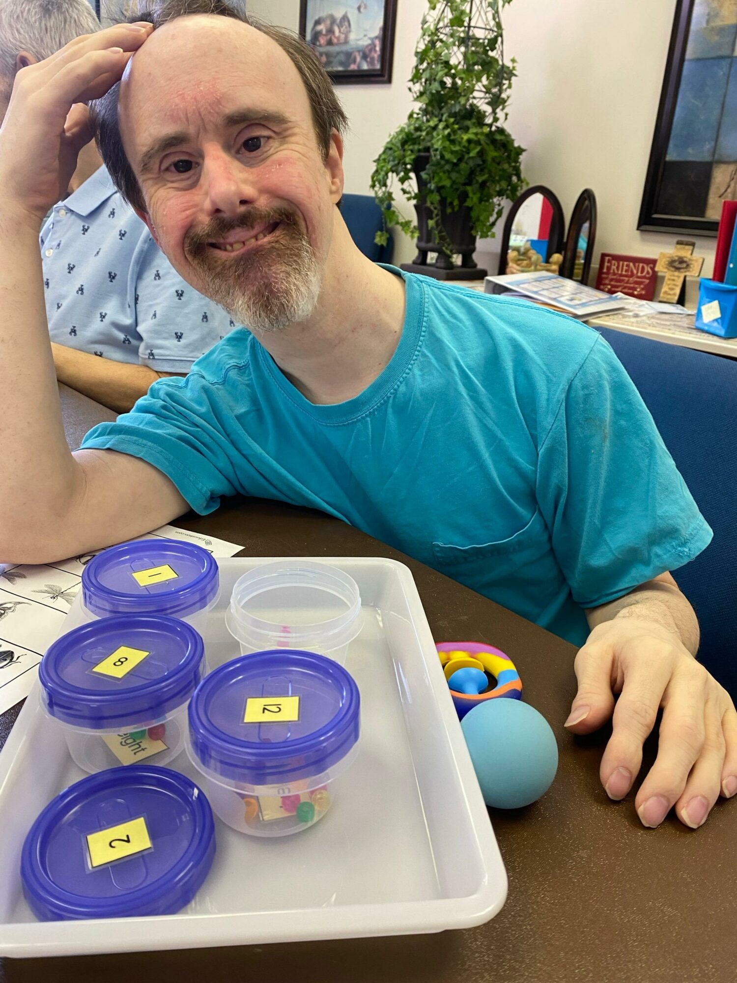 Smiling man with a beard and blue shirt sitting at a table with containers of colorful beads.