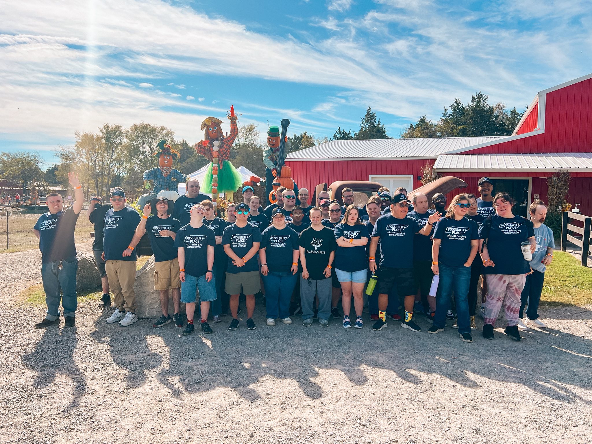Group of people standing outdoors in front of a red building and cactus decorations under a blue sky.