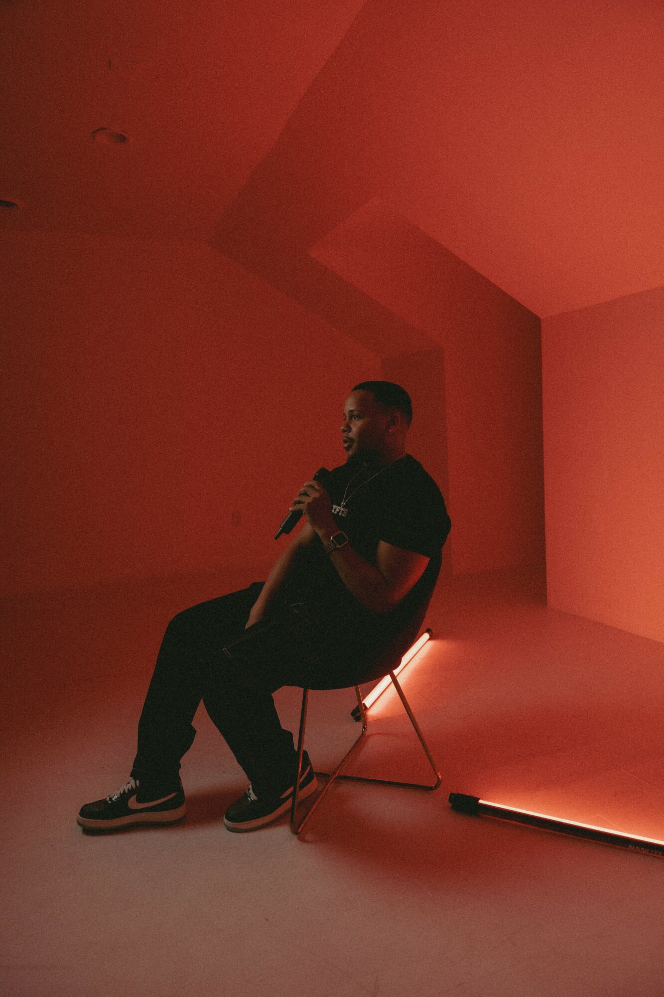 Person sitting on a chair holding a microphone in a dimly lit room with red lighting.