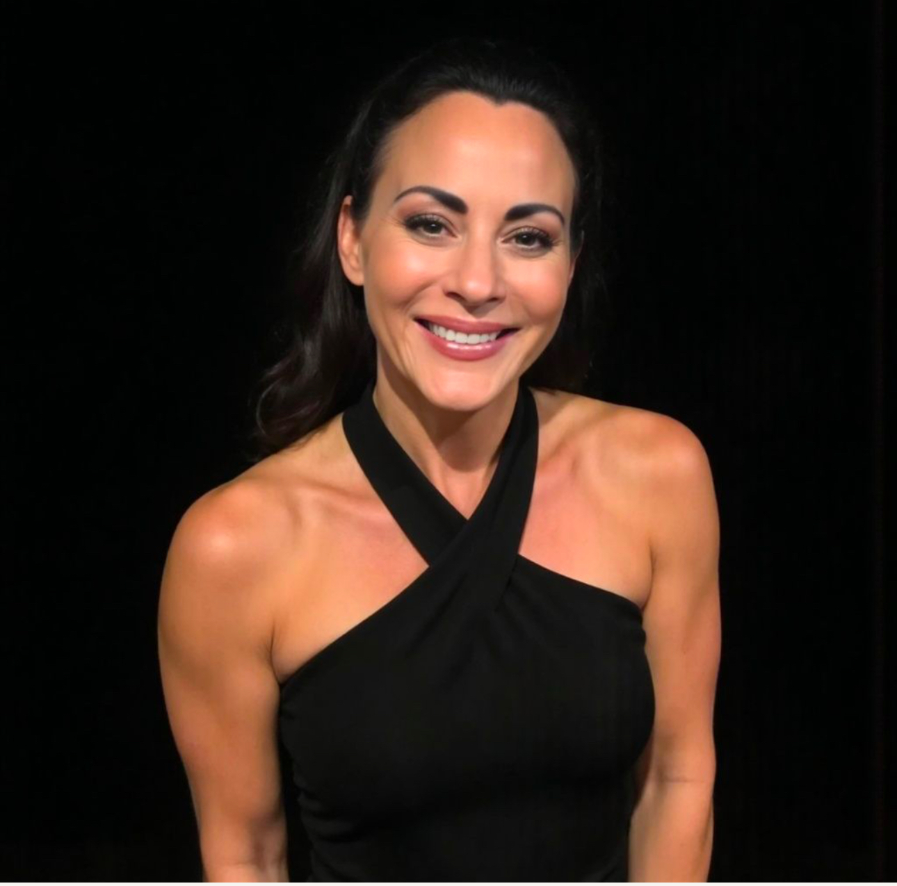 Woman with dark hair smiling, wearing a black halter top, against a dark background.