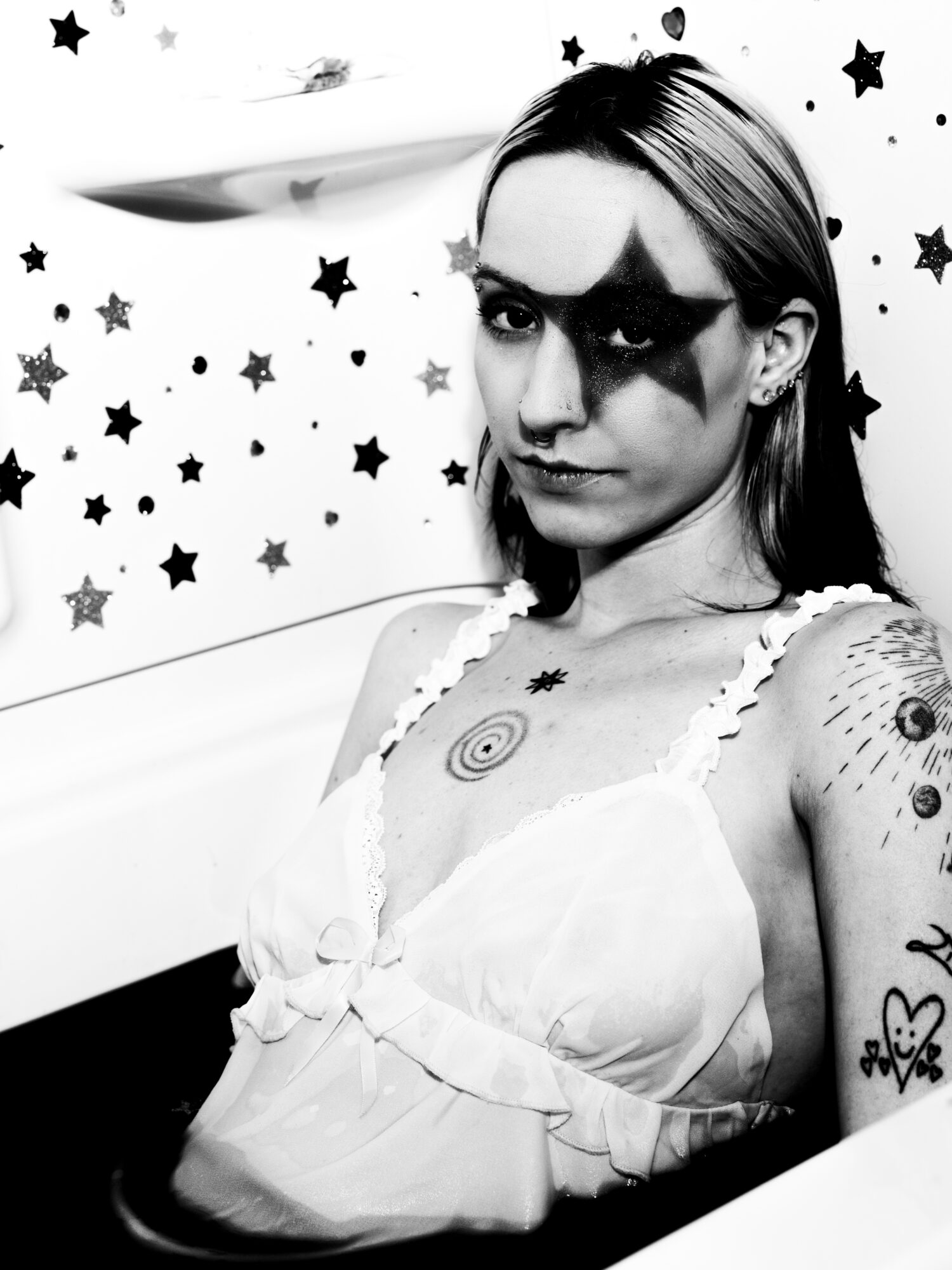 Woman with star face paint and tattoos, looking at camera, background with star decorations, black and white photo.