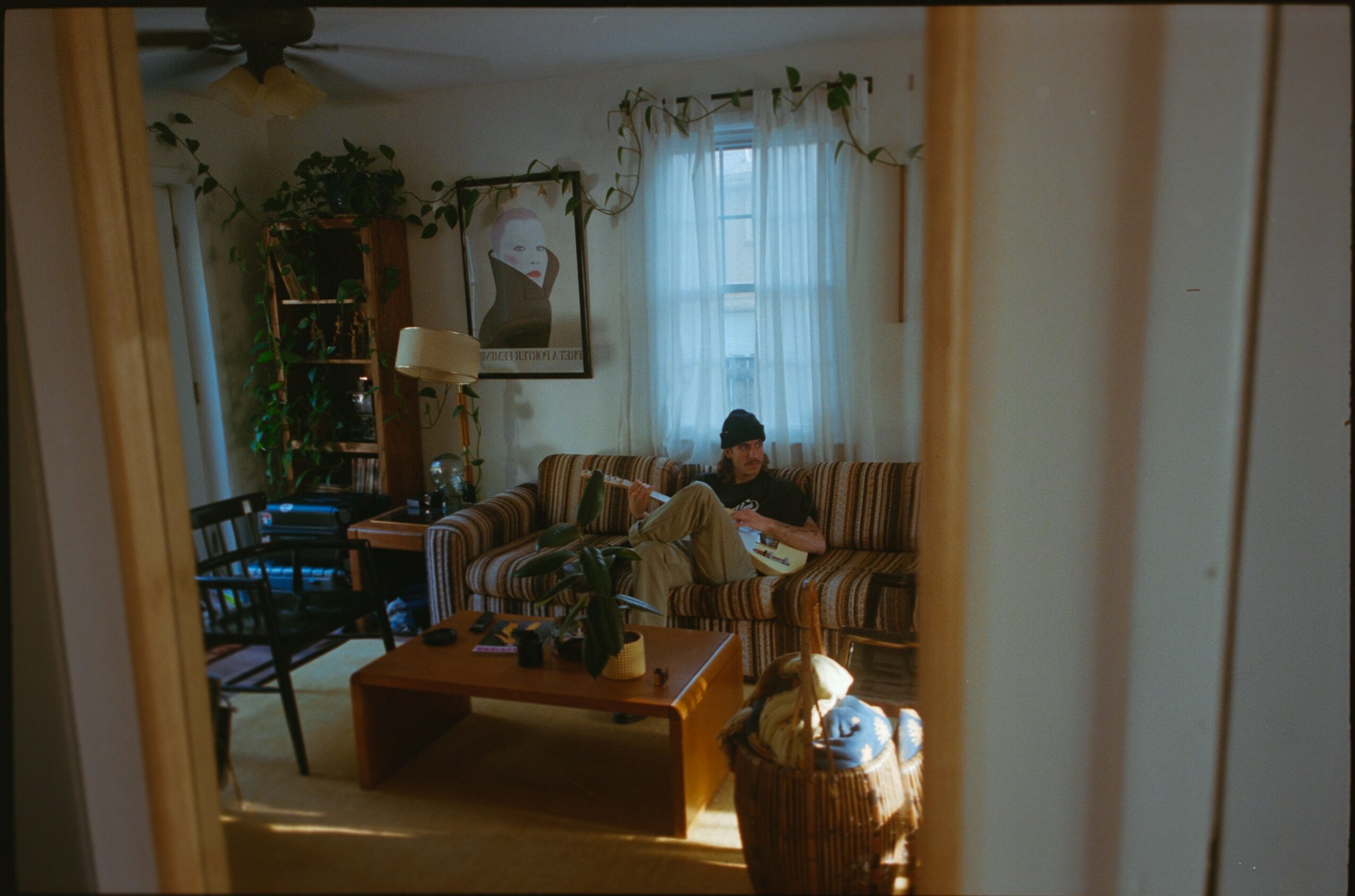 Living room with a person sitting on a striped sofa, a coffee table, and a window with curtains.