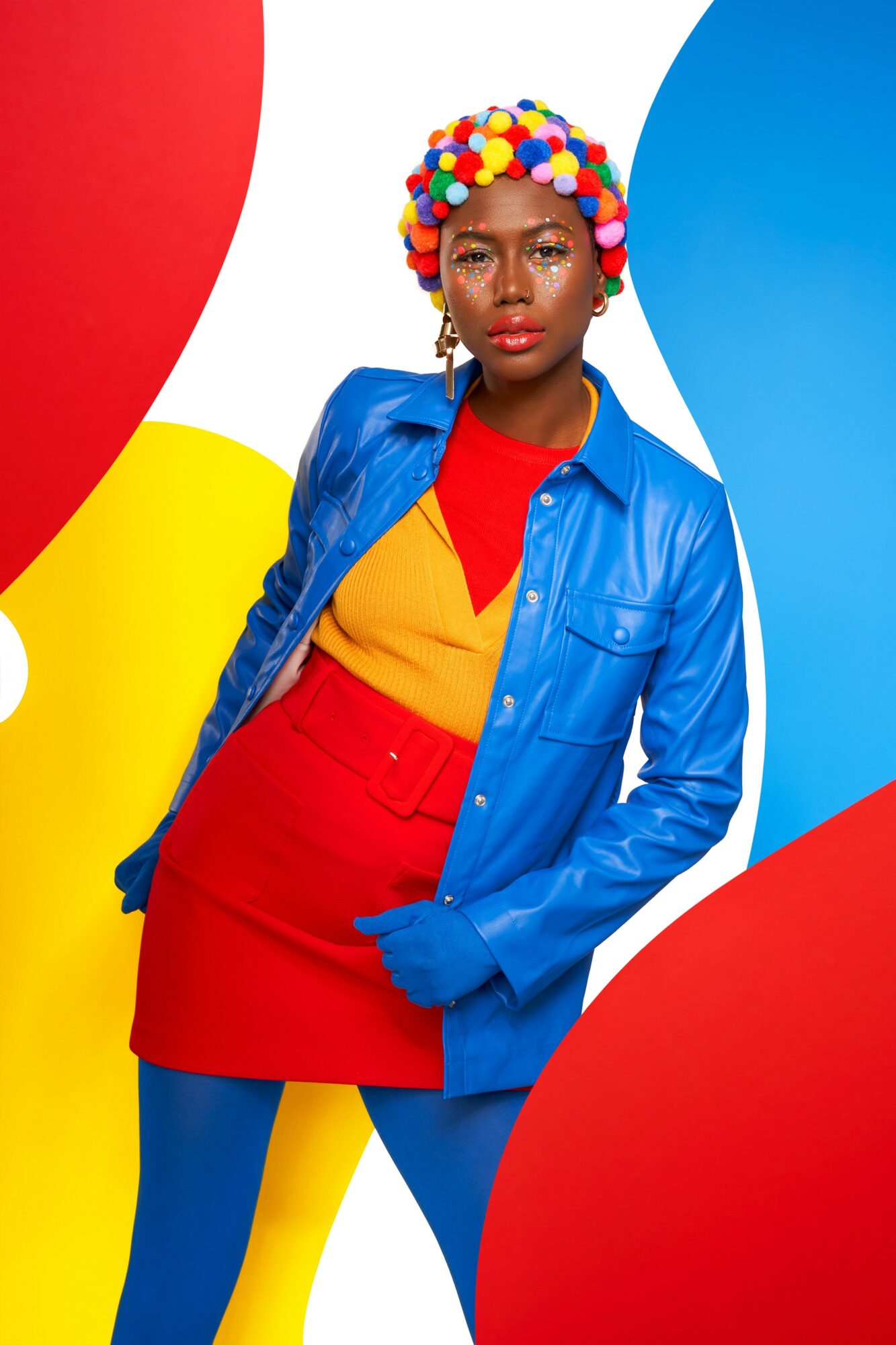 Woman with colorful pom-pom headpiece, wearing a blue jacket, red skirt, and multicolored background.