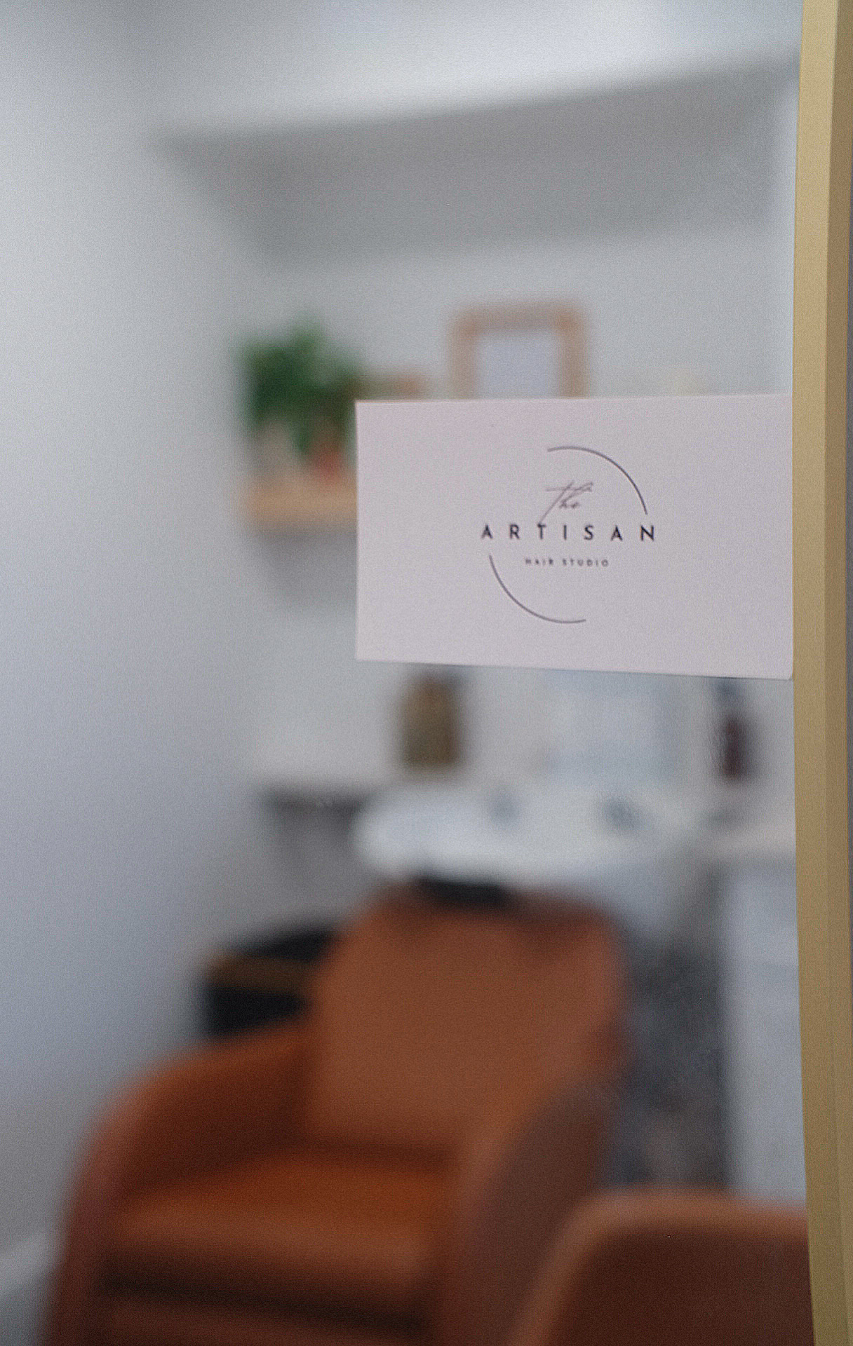 A blurred interior scene with a white wall, shelves, a plant, and a brown chair, with a white card in focus.