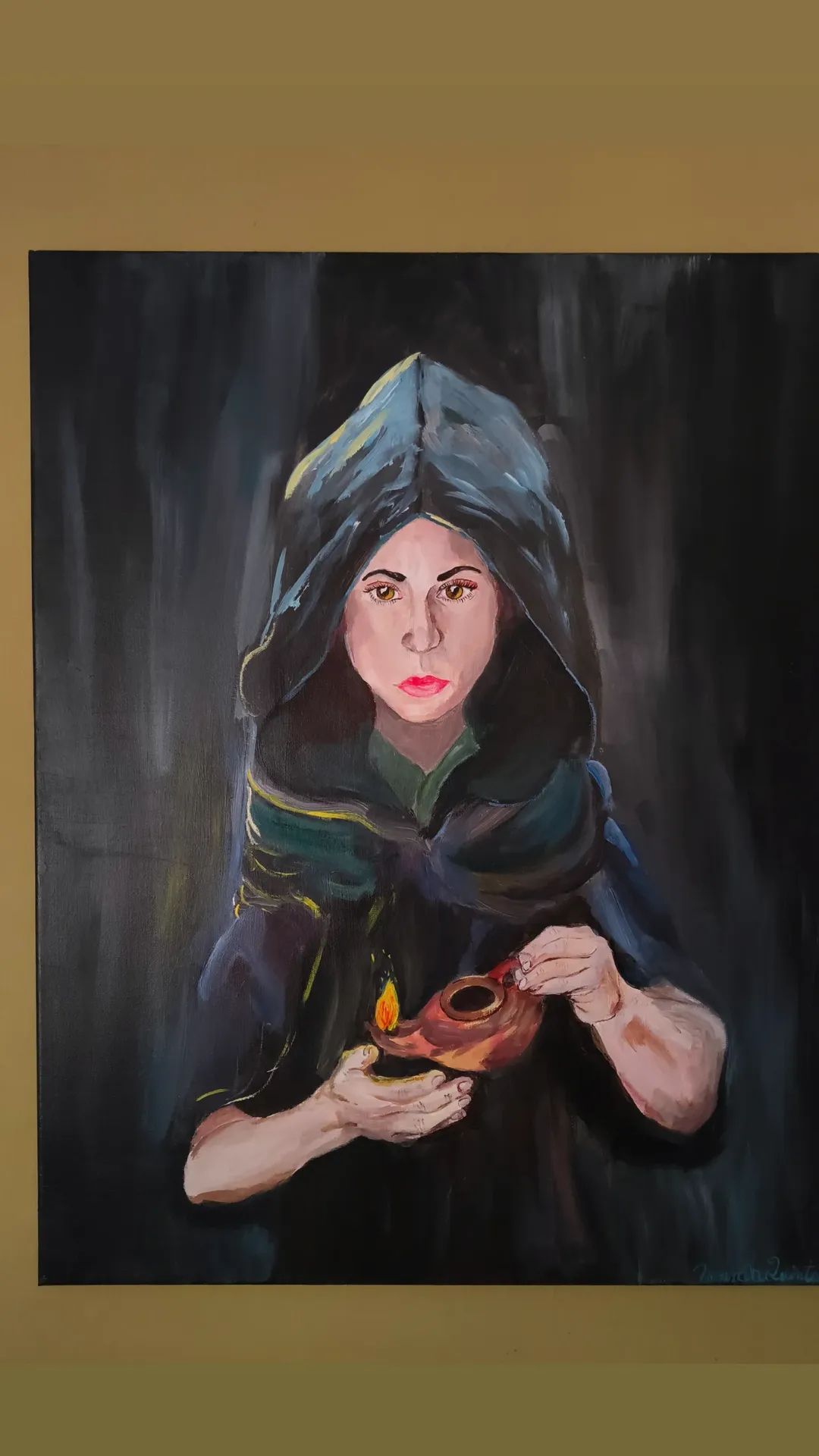 Portrait of a woman with dark hair, wearing a hooded cloak, holding a small object with a flame, against a dark background.
