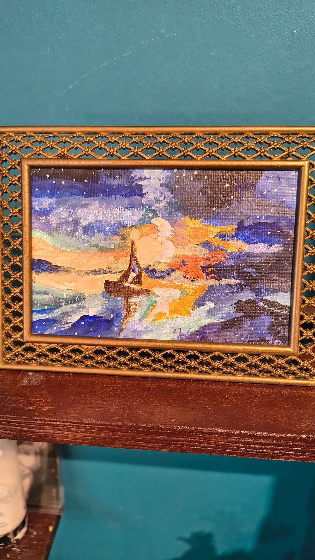 Framed painting of a sailboat on water with colorful sky, placed on a wooden surface.
