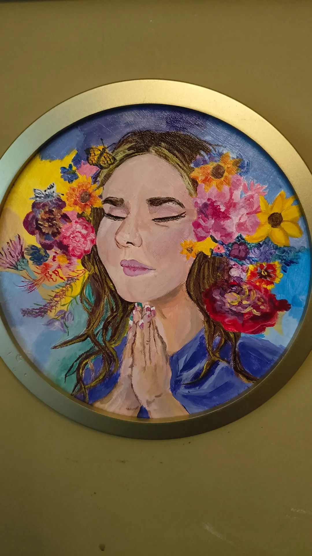Portrait of a woman with closed eyes and hands in prayer, surrounded by colorful flowers, in a circular frame.