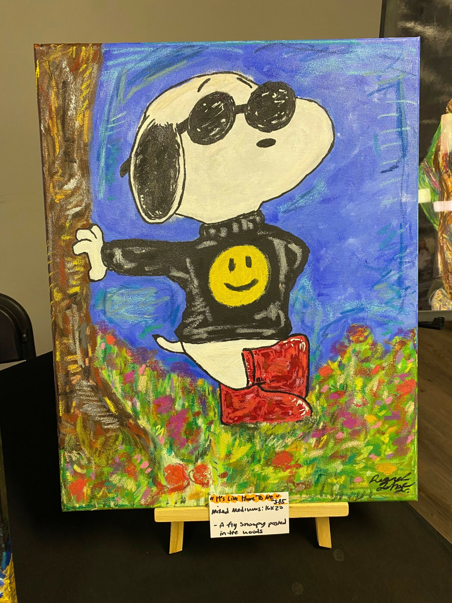 Painting of a black and white cartoon dog with a yellow face, standing on a colorful background with trees and sky.