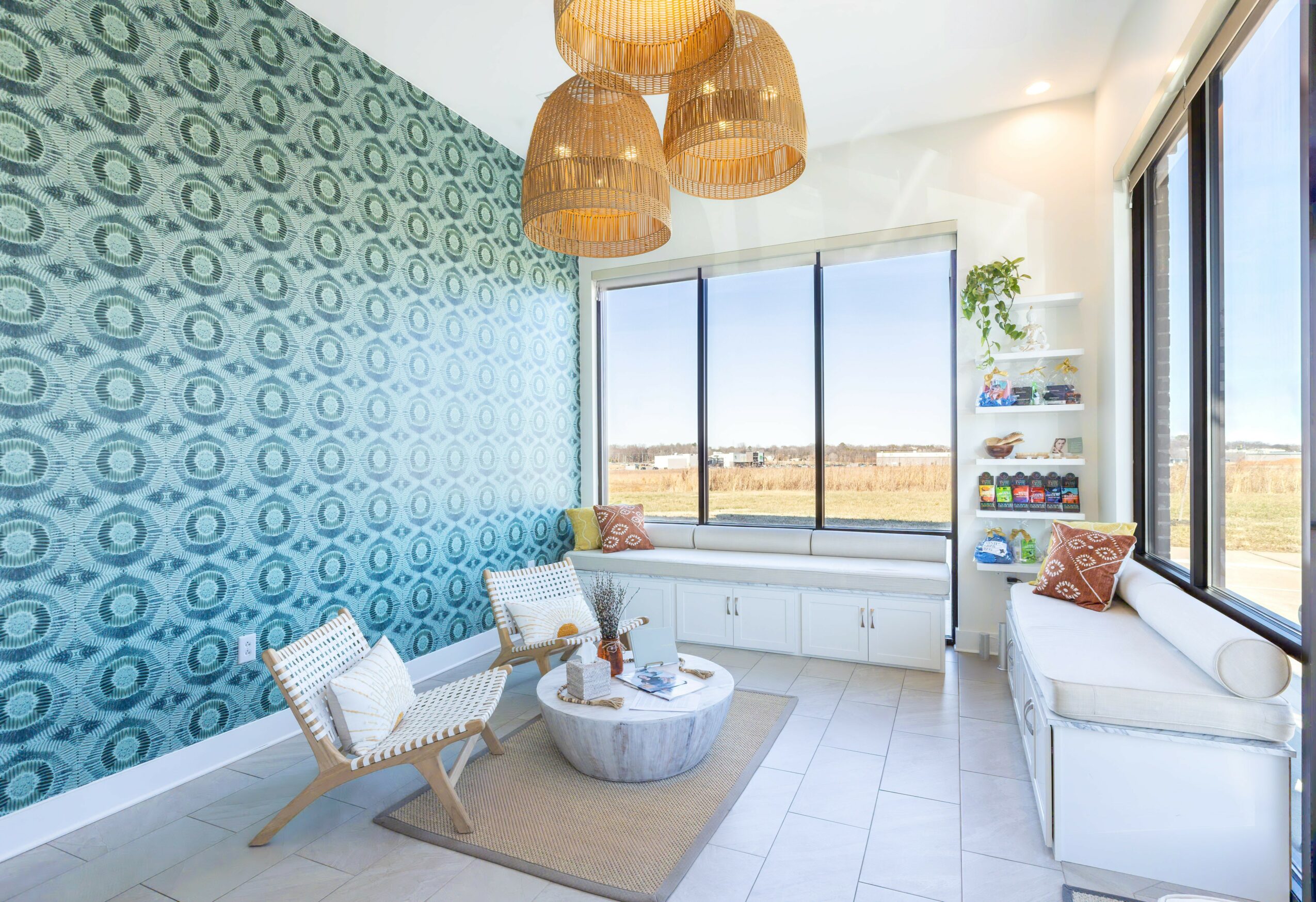 Bright room with large windows, patterned blue wall, white furniture, and hanging pendant lights, overlooking a landscape.