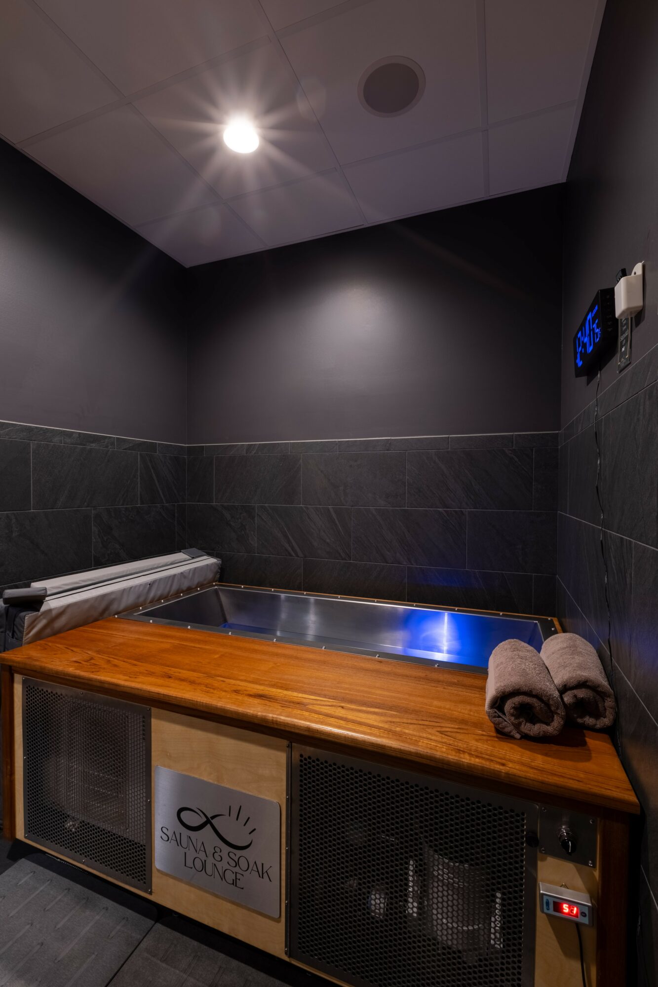 Indoor room with dark walls, ceiling light, and a wooden counter with rolled towels and a small refrigerator.