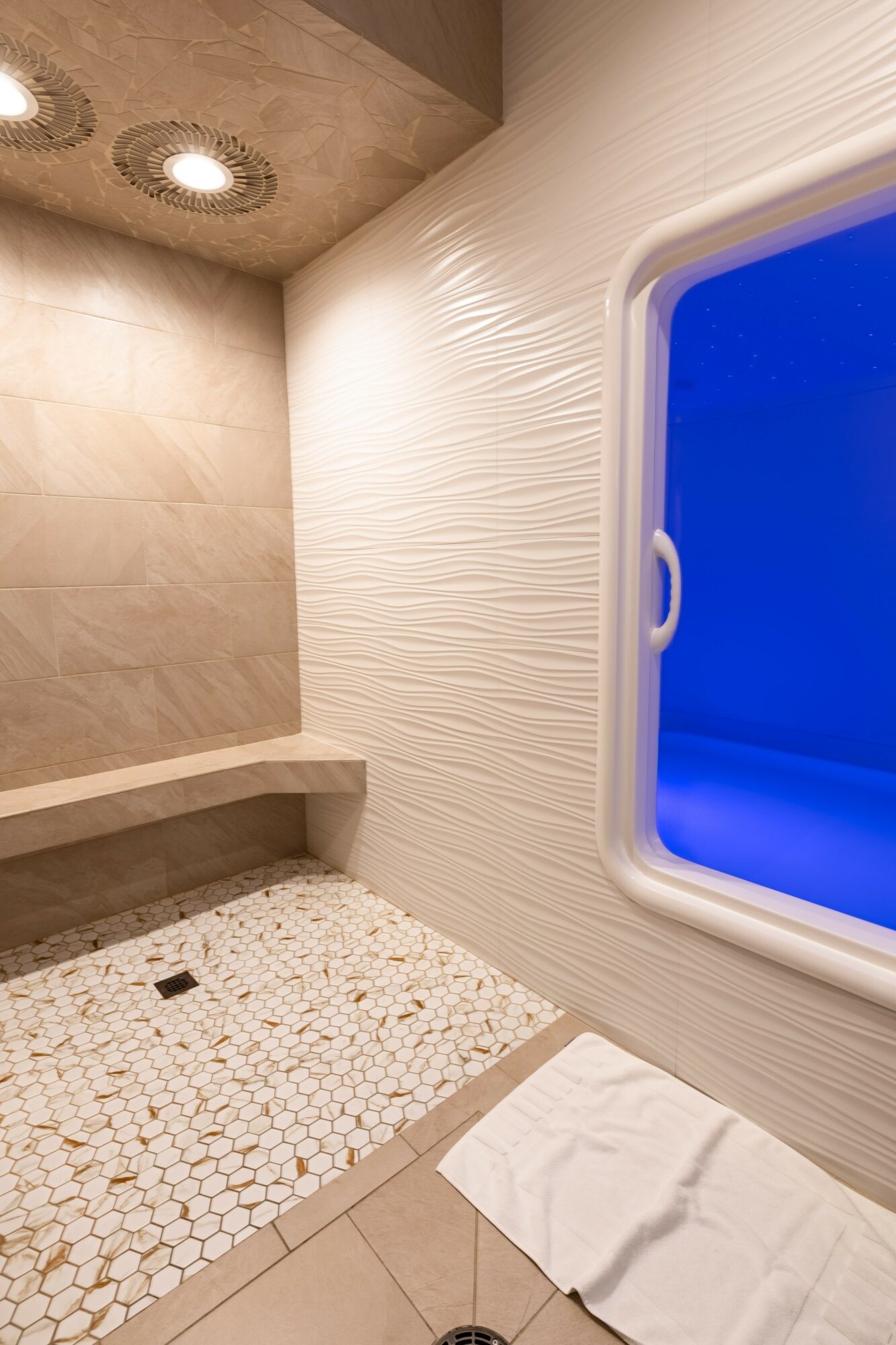 Bathroom with a window, textured wall, tiled floor, and a towel on the floor.