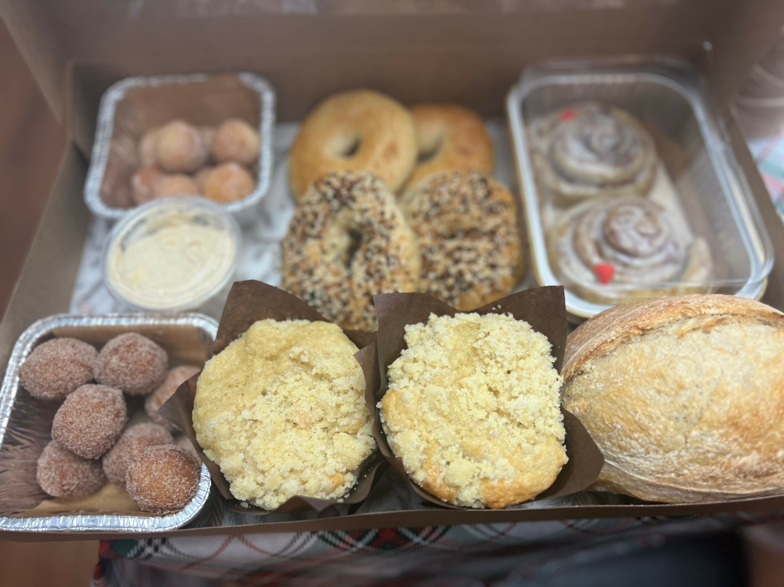 Assorted baked goods including cookies, bread, and pastries in a box, with some items in foil containers and paper cups.