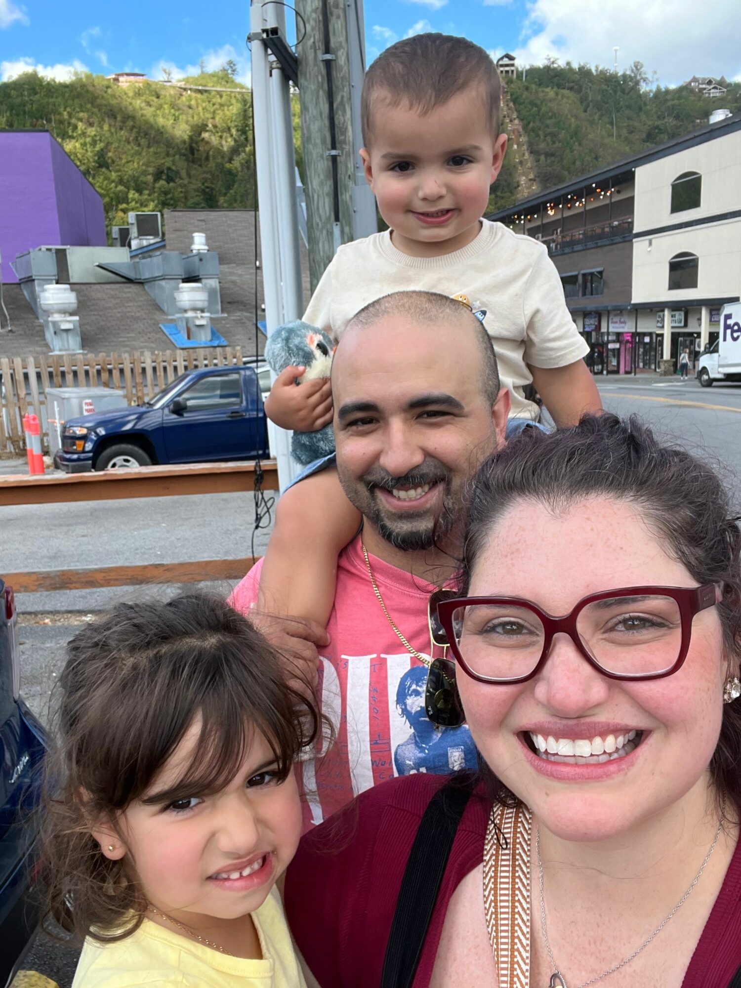 Four people smiling outdoors, two children and two adults, with a boat and trees in the background.