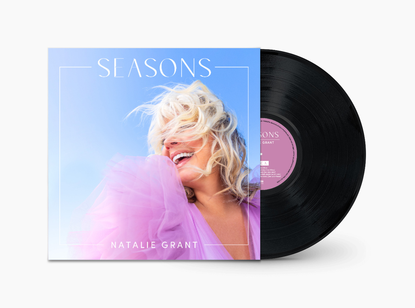 Vinyl record partially pulled out of album cover featuring a smiling woman with blonde hair, pink and purple clothing, and a blue sky background.