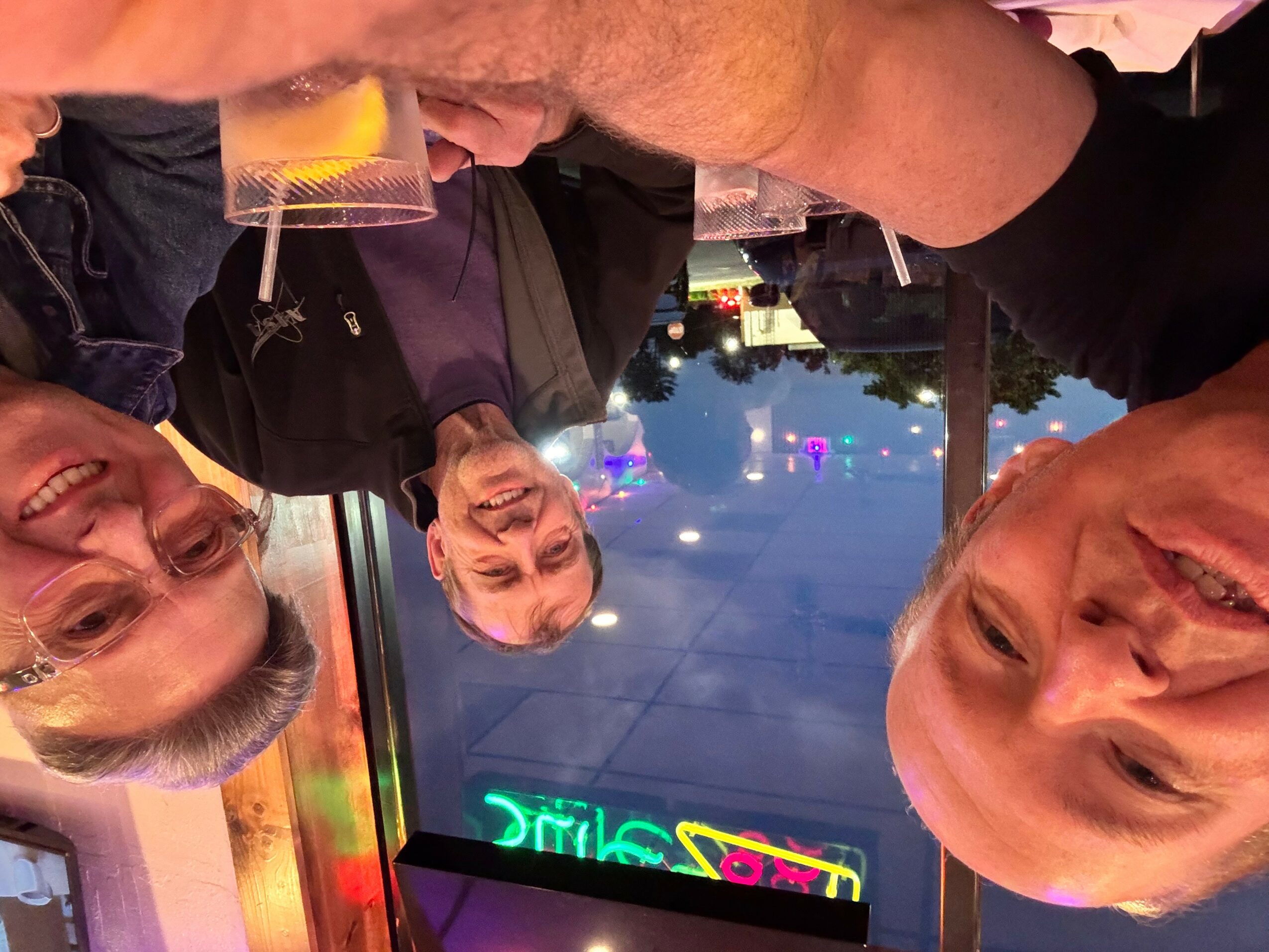 Three people smiling outdoors at night with a neon sign in the background.