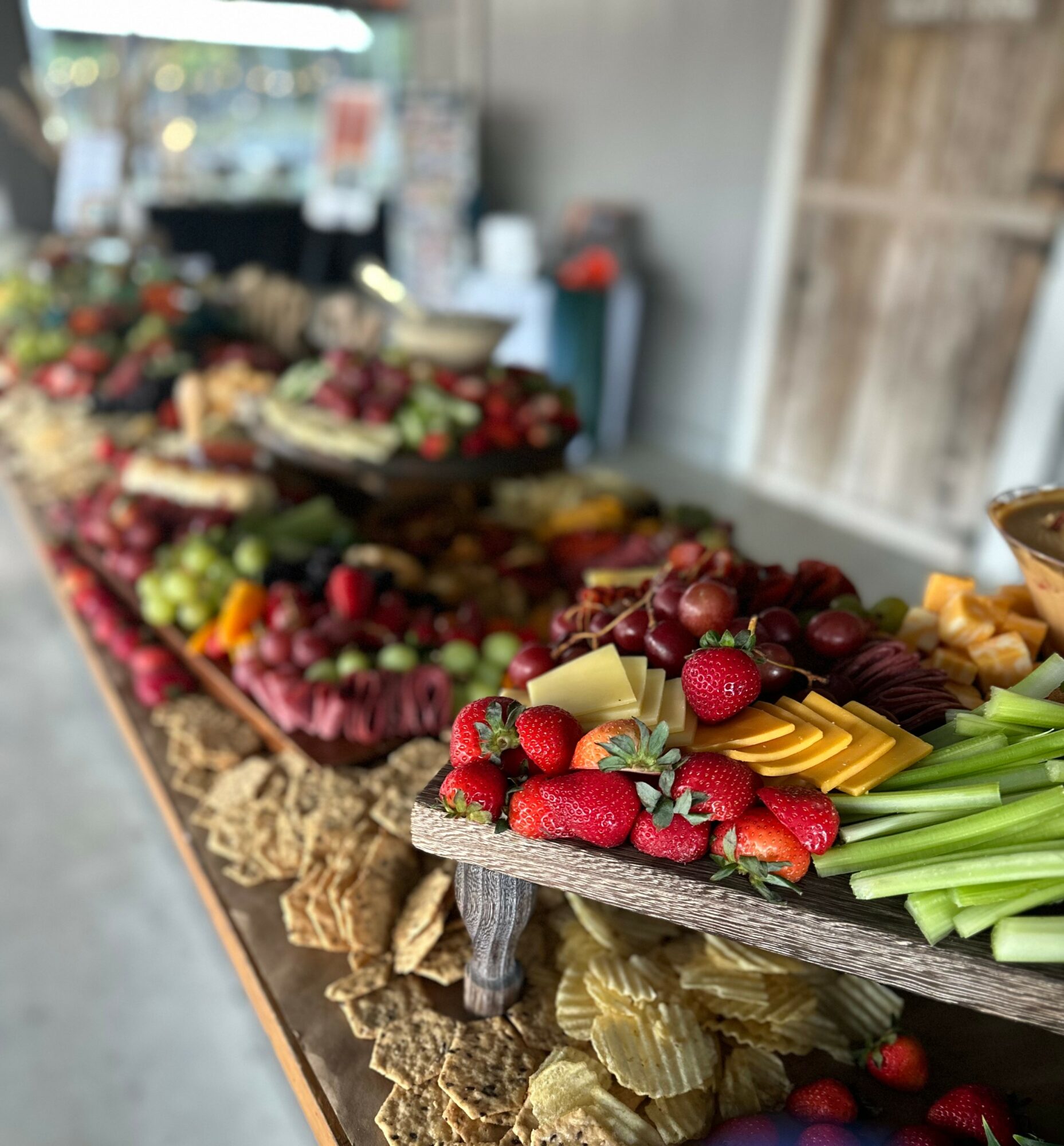 Display of various fresh fruits on a wooden table, including strawberries, grapes, and other produce, in an outdoor market setting.
