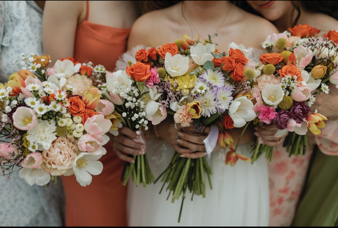 Group of women holding colorful bouquets of flowers, with only their torsos visible, in a wedding or celebration setting.