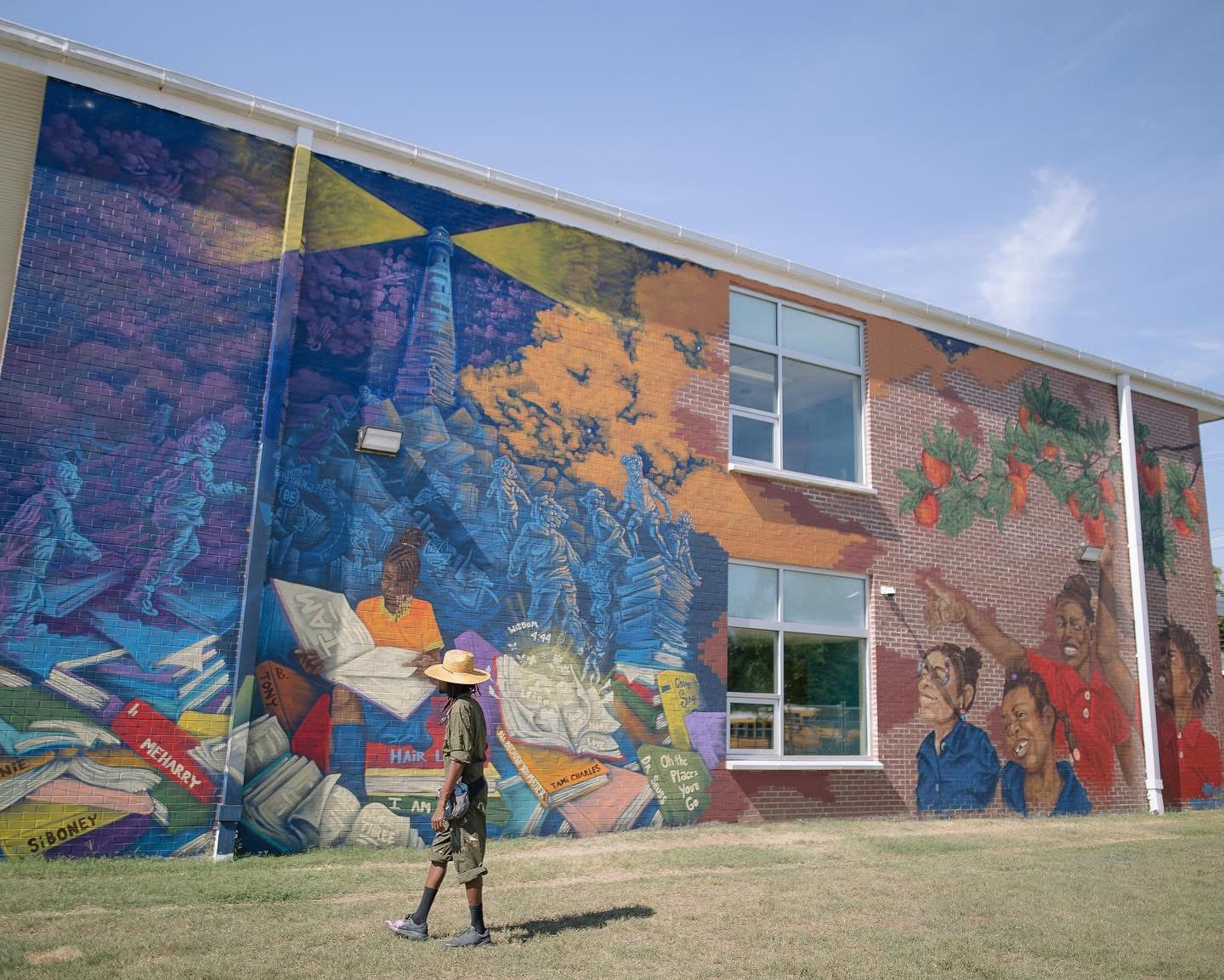 Person walking past a colorful mural on a building with two windows, blue sky above.