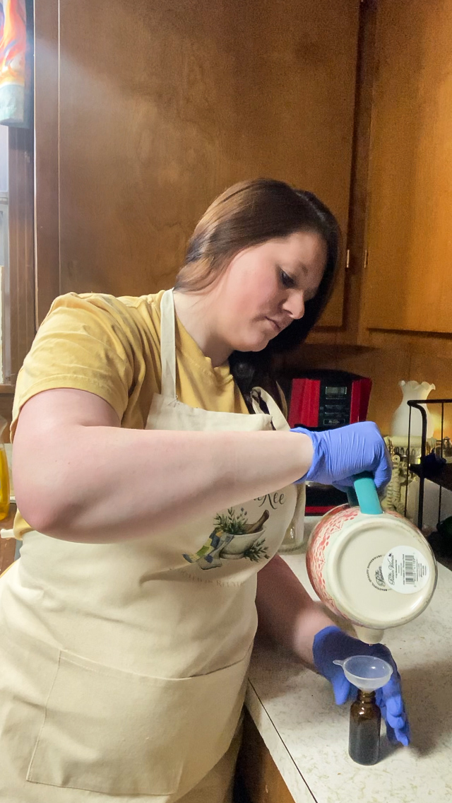 Woman in yellow shirt and apron holding a container in a kitchen, wearing blue gloves, with wooden cabinets in background.
