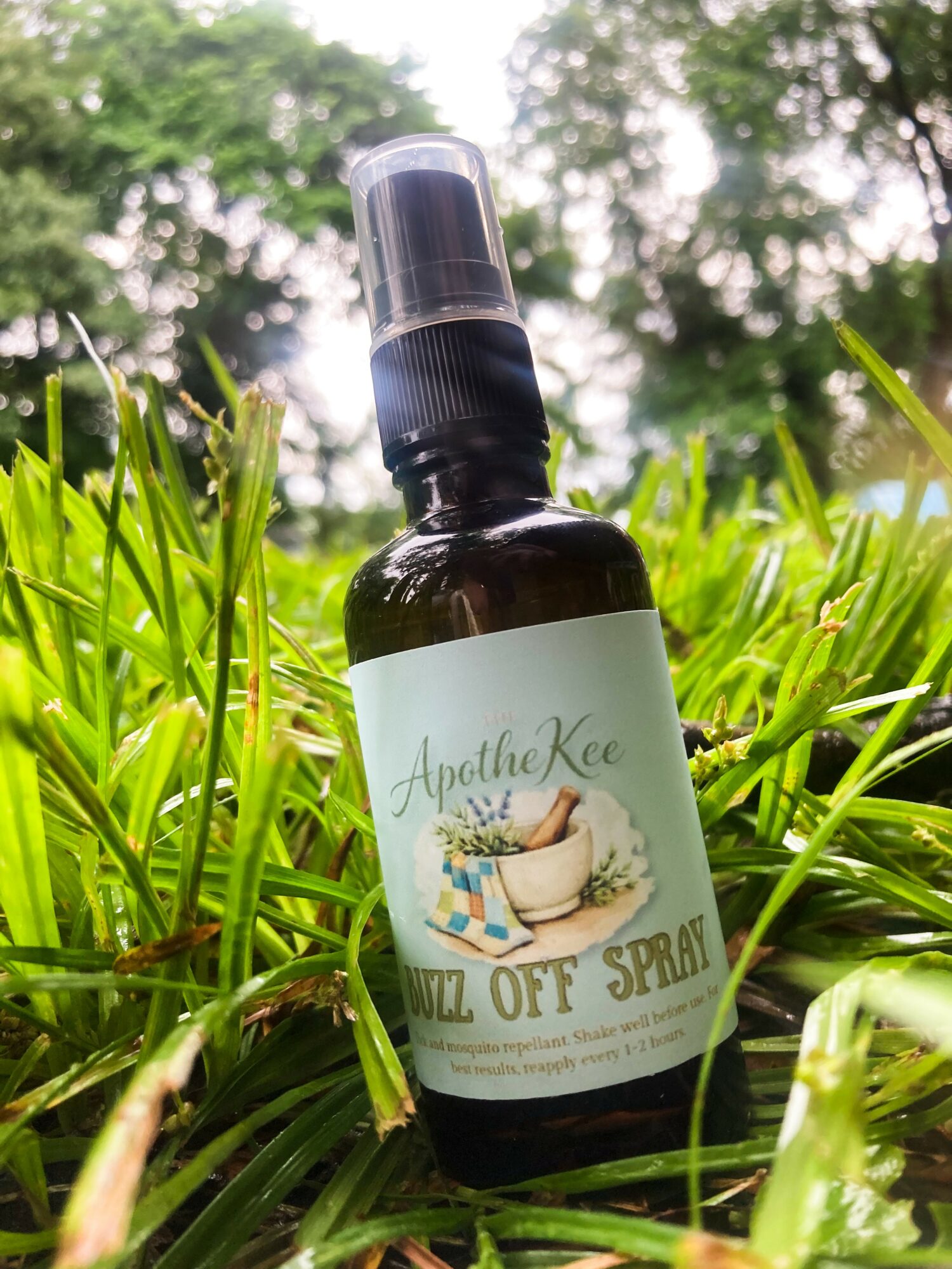 Dark spray bottle with a white label featuring a bathtub and flowers, placed on green grass outdoors.