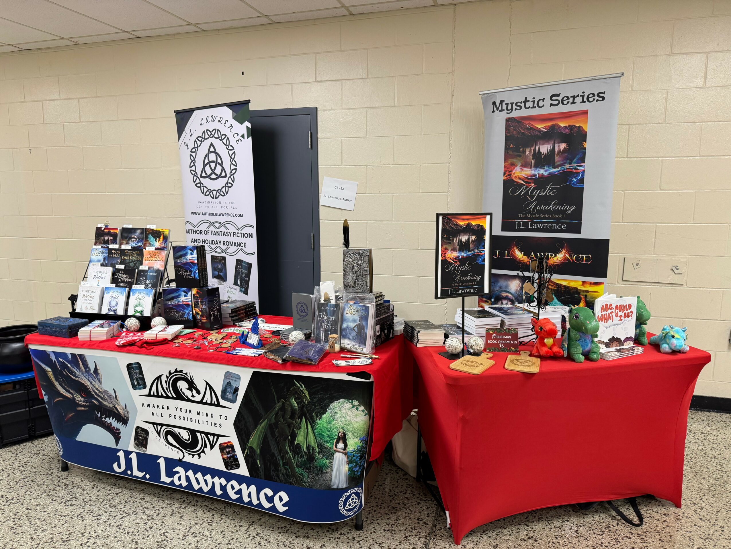 Two tables with promotional materials and displays, one with a black and white banner, the other with a Mystic Series poster, set against a beige wall.
