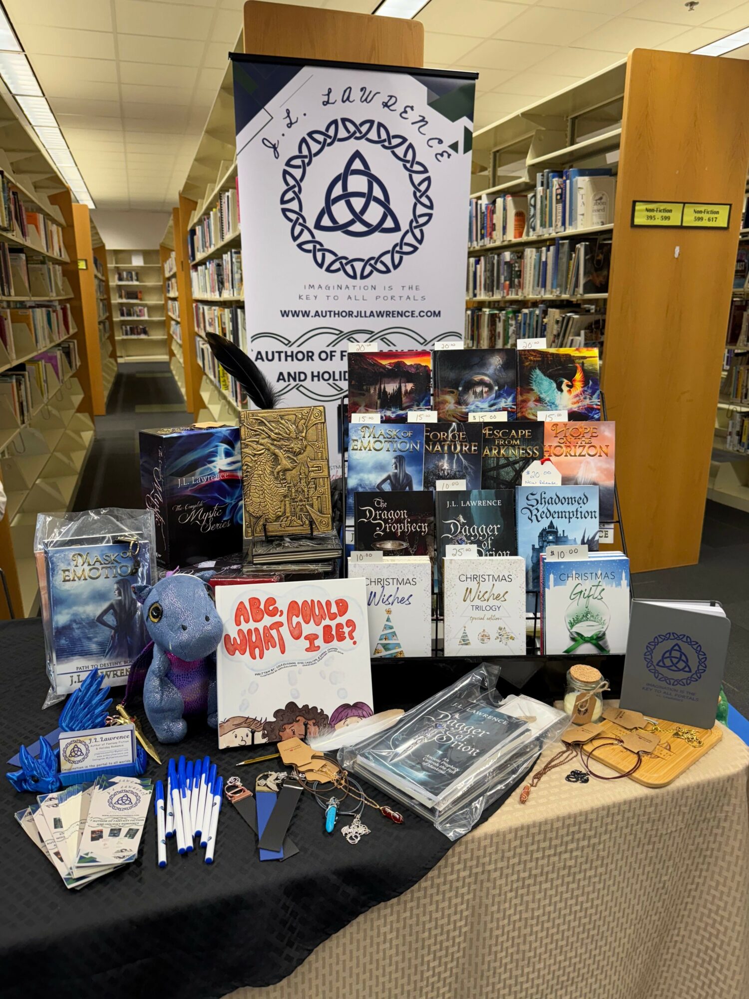 Books and promotional materials on a table in a library, with a bookshelf in the background, and a banner with a logo.