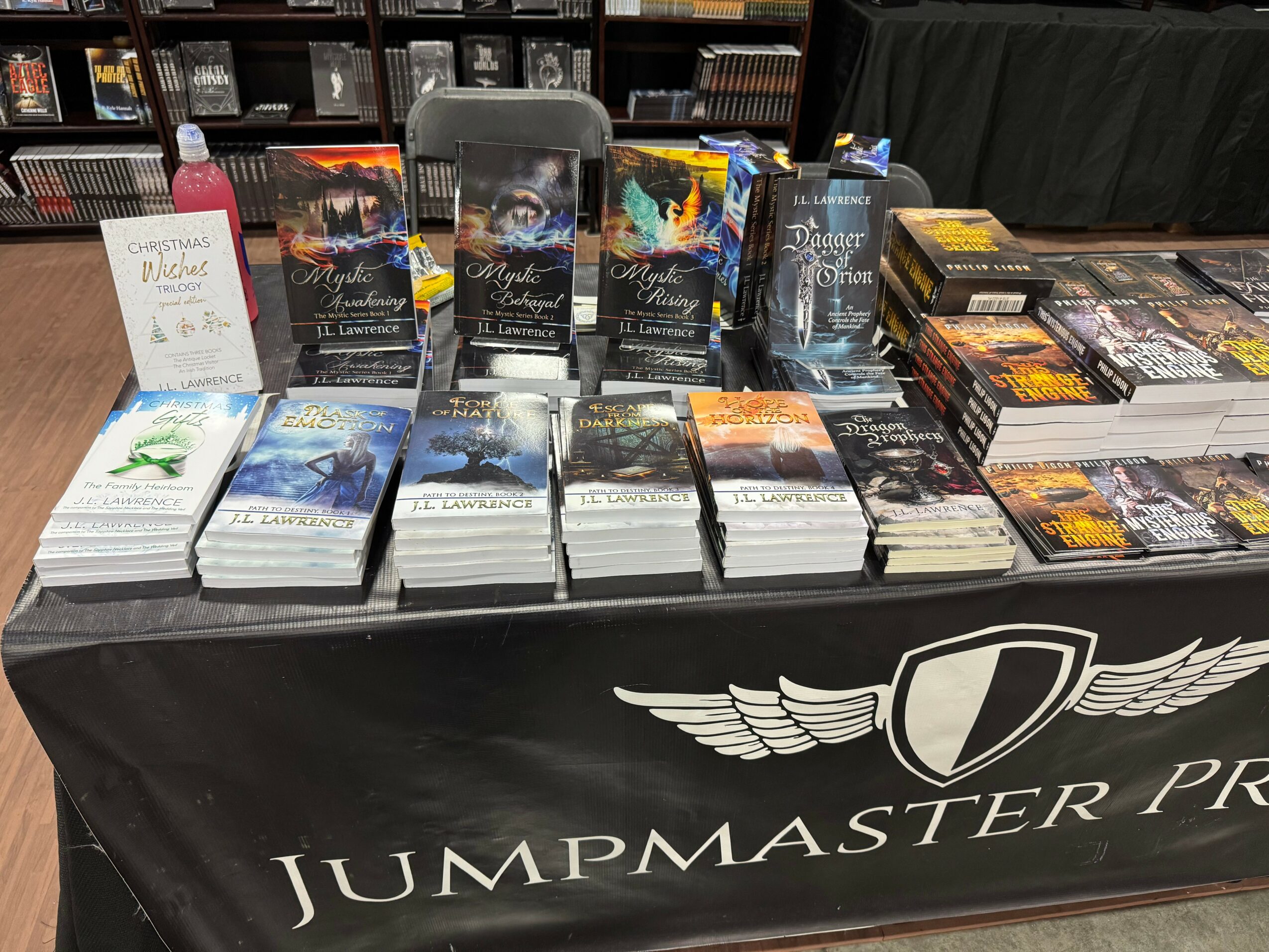 Table with multiple stacks of books and promotional materials, covered with a black cloth displaying the JumpMaster logo.