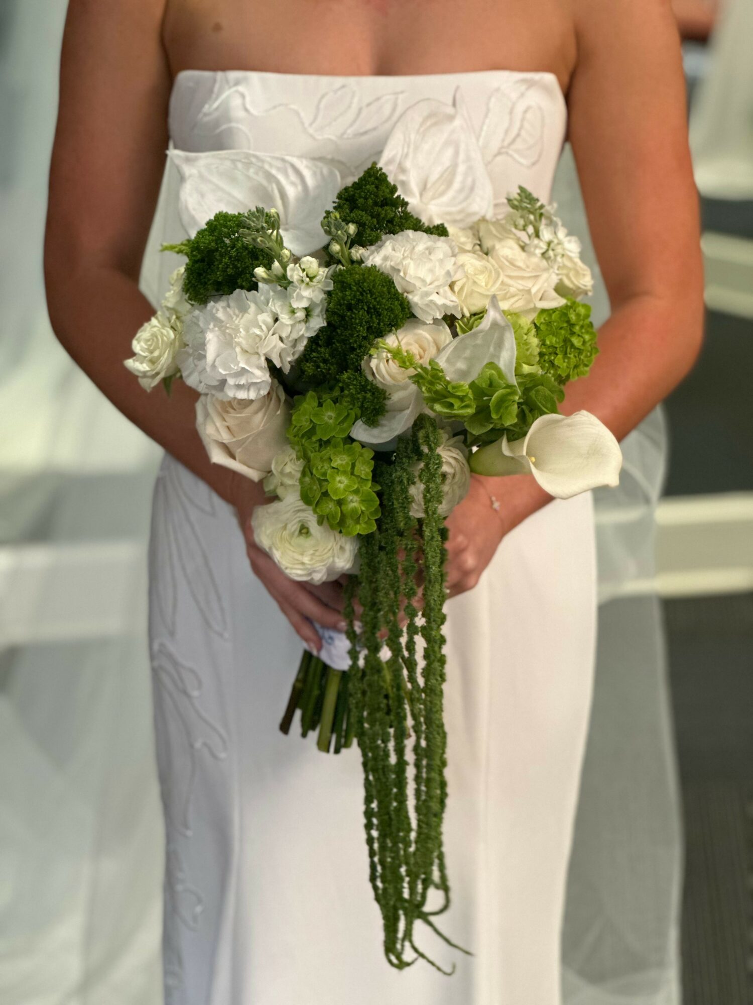 Person in white dress holding a large bouquet of white and green flowers, with a white wrist corsage.