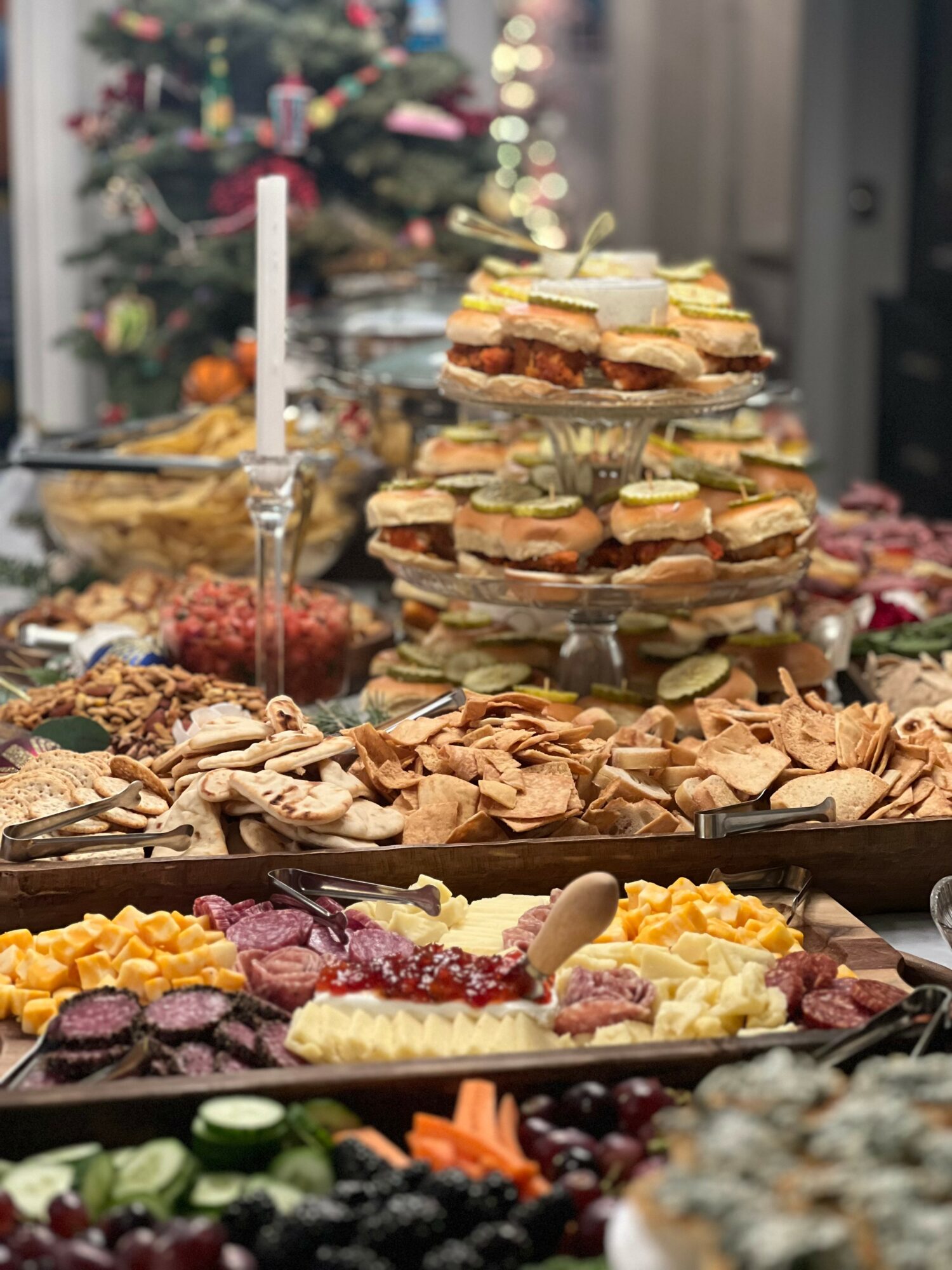Assorted desserts and snacks on a table with a decorated Christmas tree in the background.