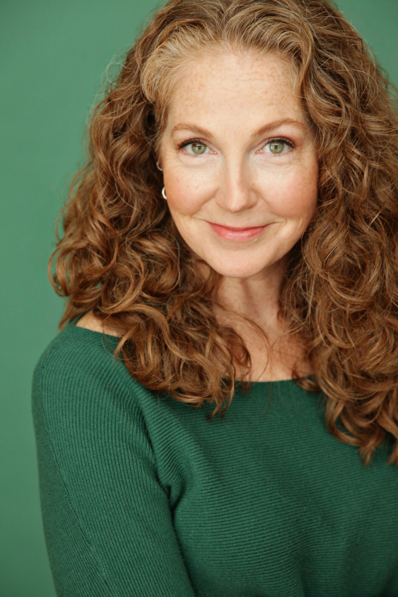 Woman with curly hair smiling, wearing a green top, against a green background.