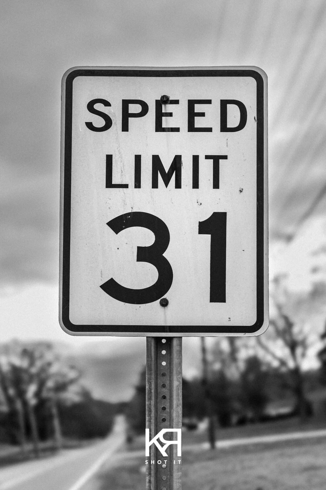 Speed limit sign showing 31 miles per hour, with trees and power lines in the background.