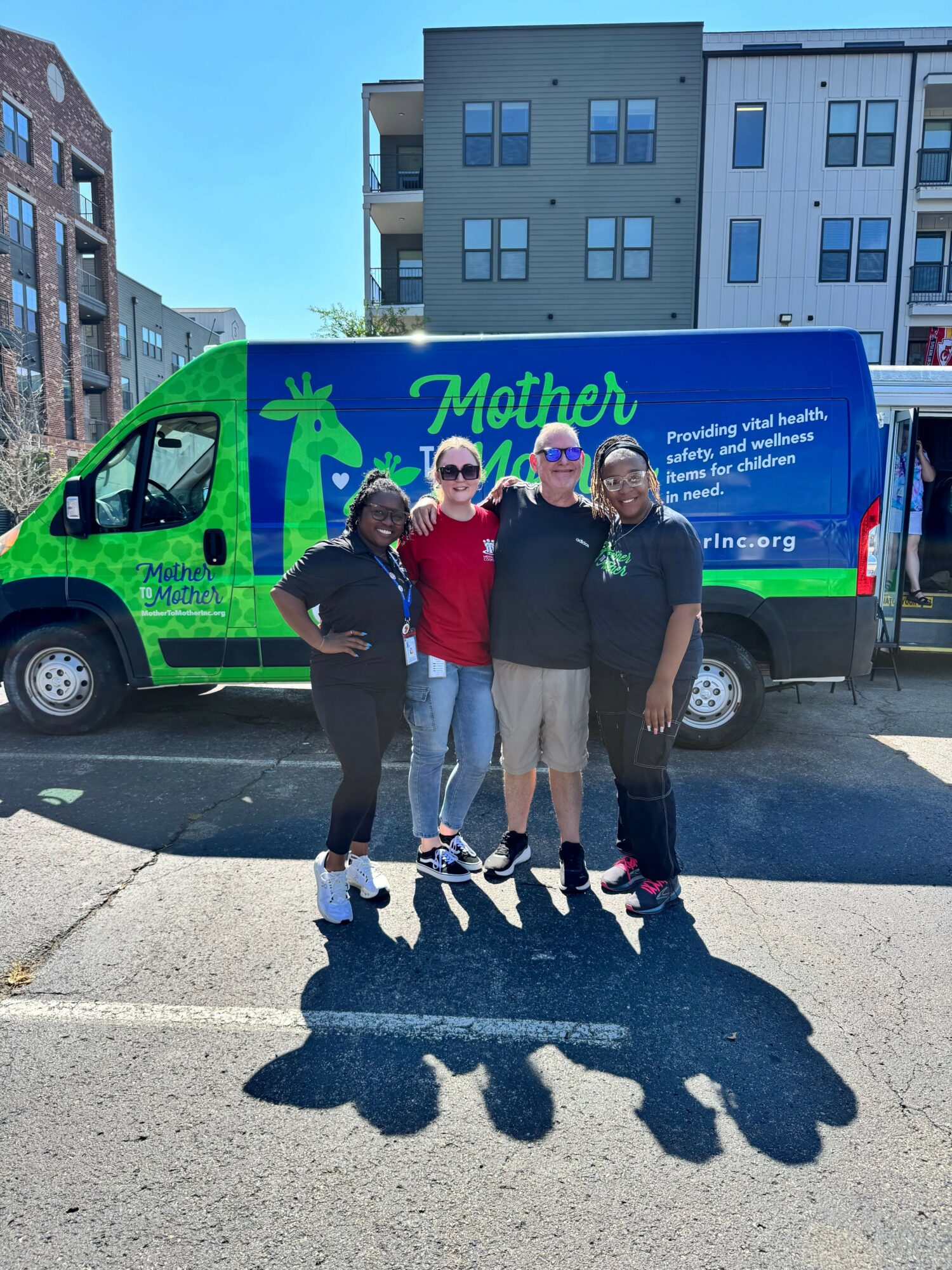 Three people standing on a sidewalk in front of a colorful bus with children and text, casting shadows on the ground.