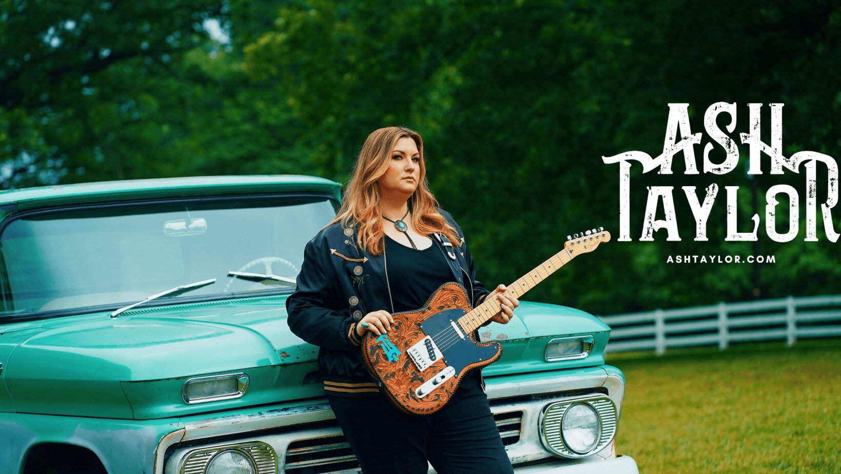 Woman with a guitar leaning against a vintage green car outdoors, trees and a white fence in background.