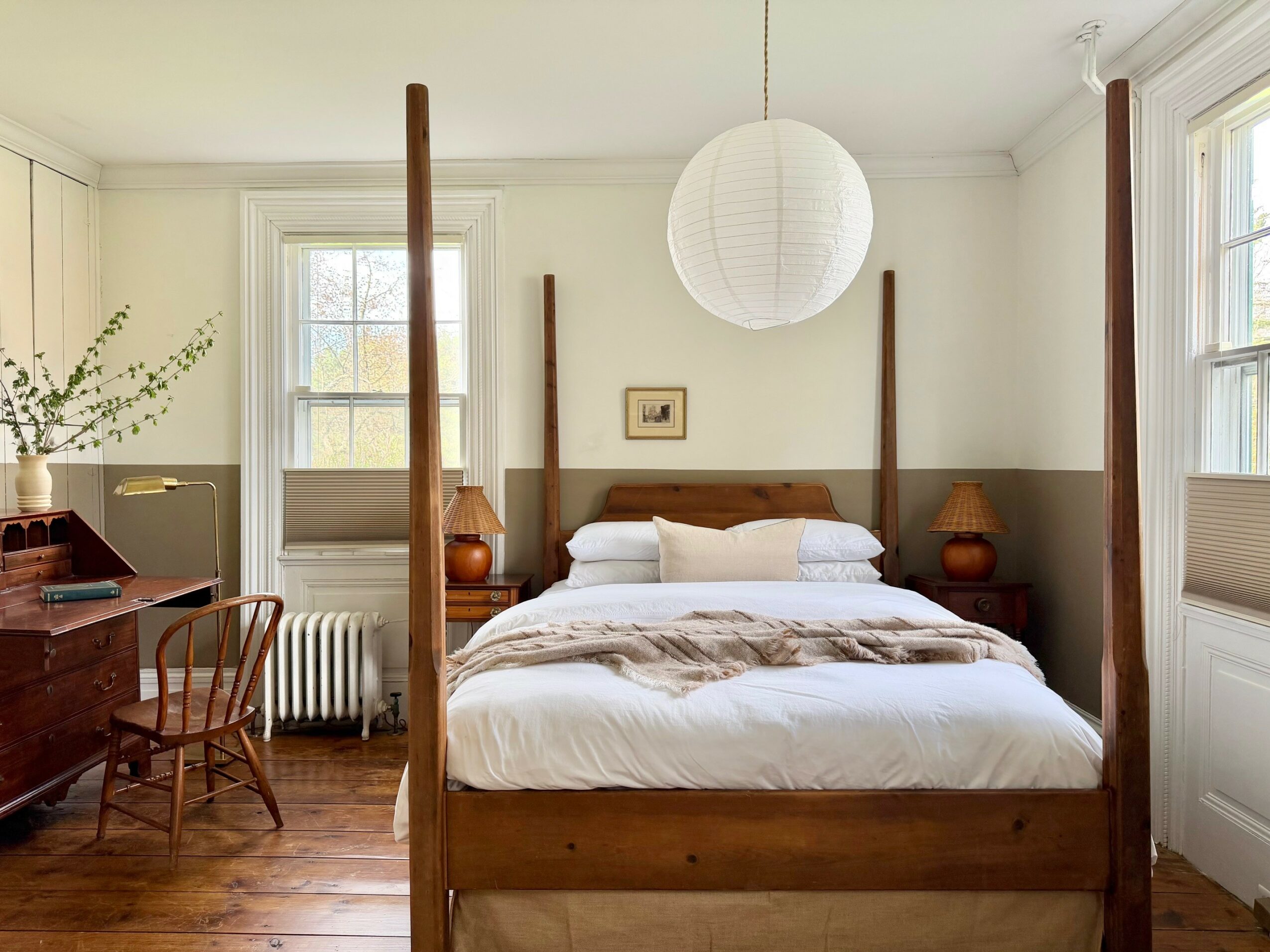 Upright bedroom with a wooden four-poster bed, white bedding, two bedside lamps, a paper lantern, and a window with natural light.
