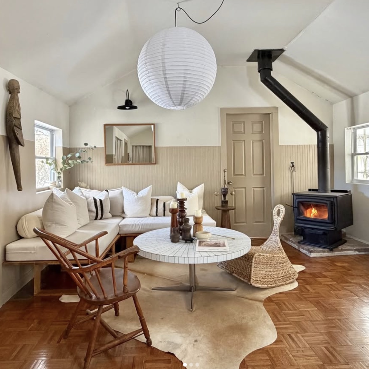 Cozy living room with a white sofa, round coffee table, wood chair, and a wood stove in the corner.