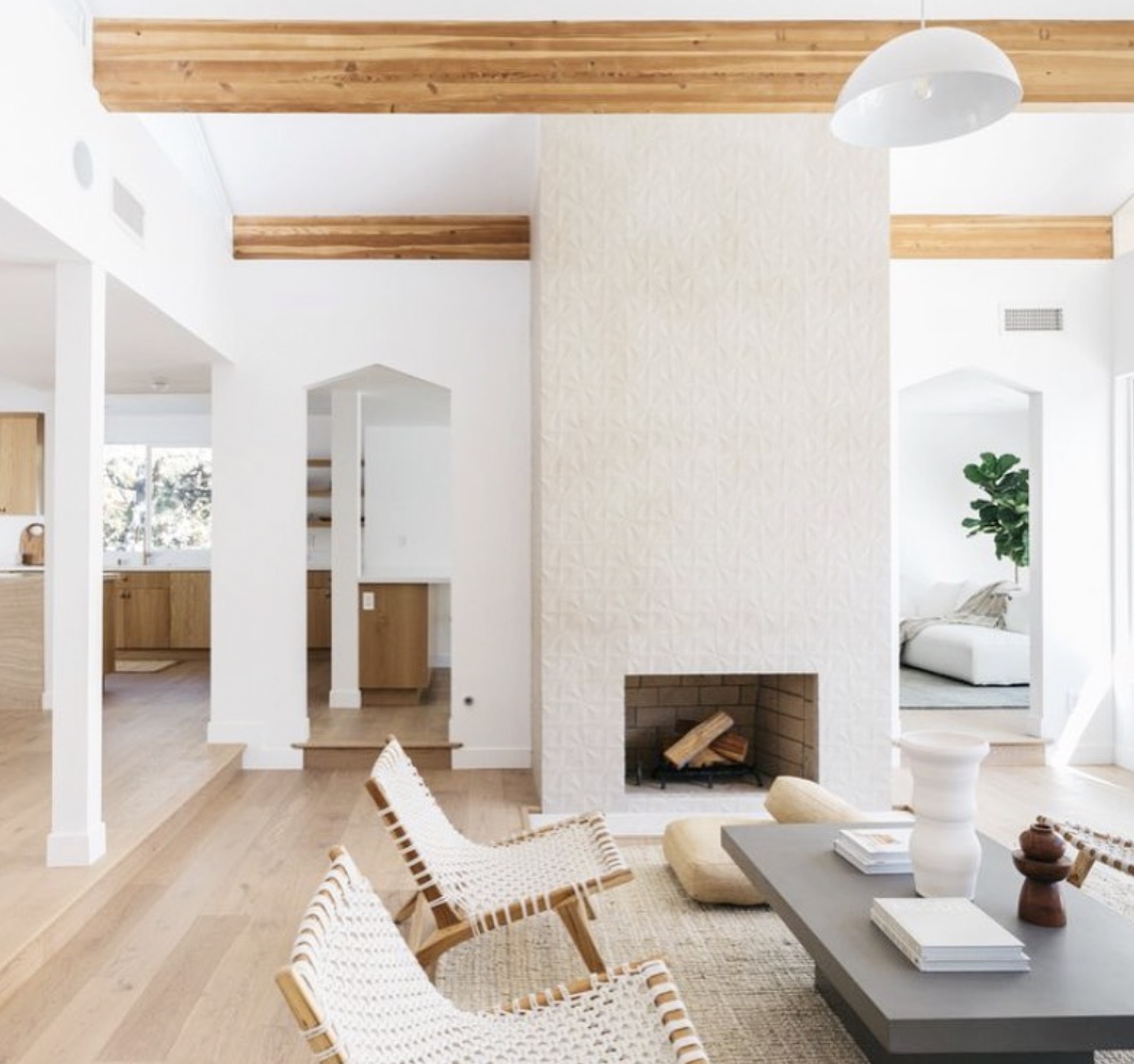 Living room with white walls, wooden ceiling beams, a fireplace, and modern furniture including chairs and a coffee table.