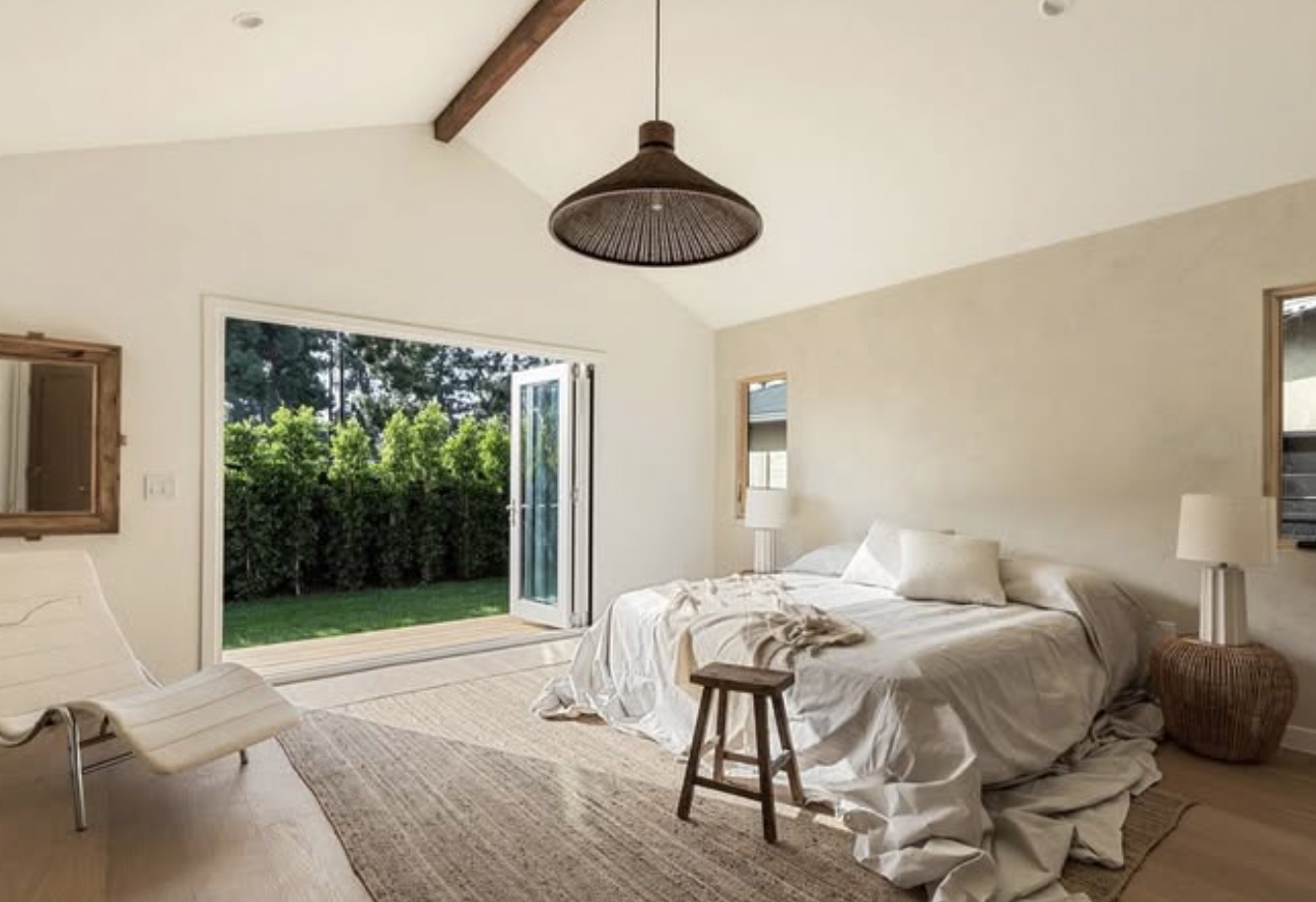 Bedroom with bed, open door to garden, white walls, and minimal decor.