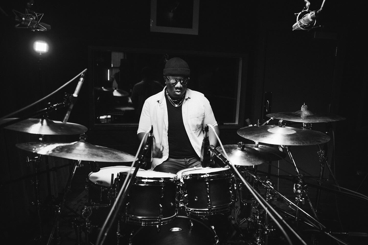Person playing drums in a recording studio with microphones and equipment, black and white image.