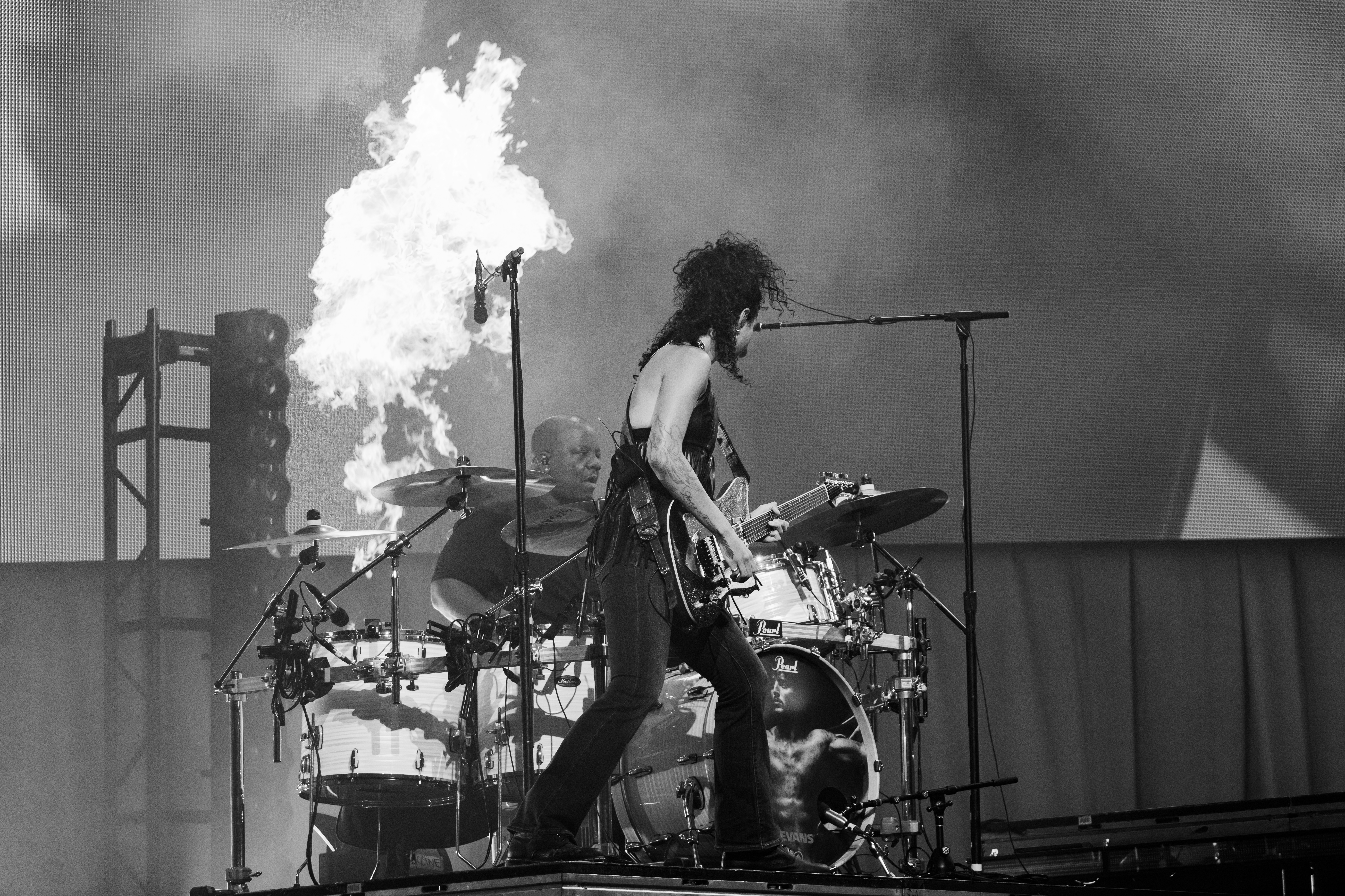 Musician playing guitar on stage with drums and smoke effects in background.