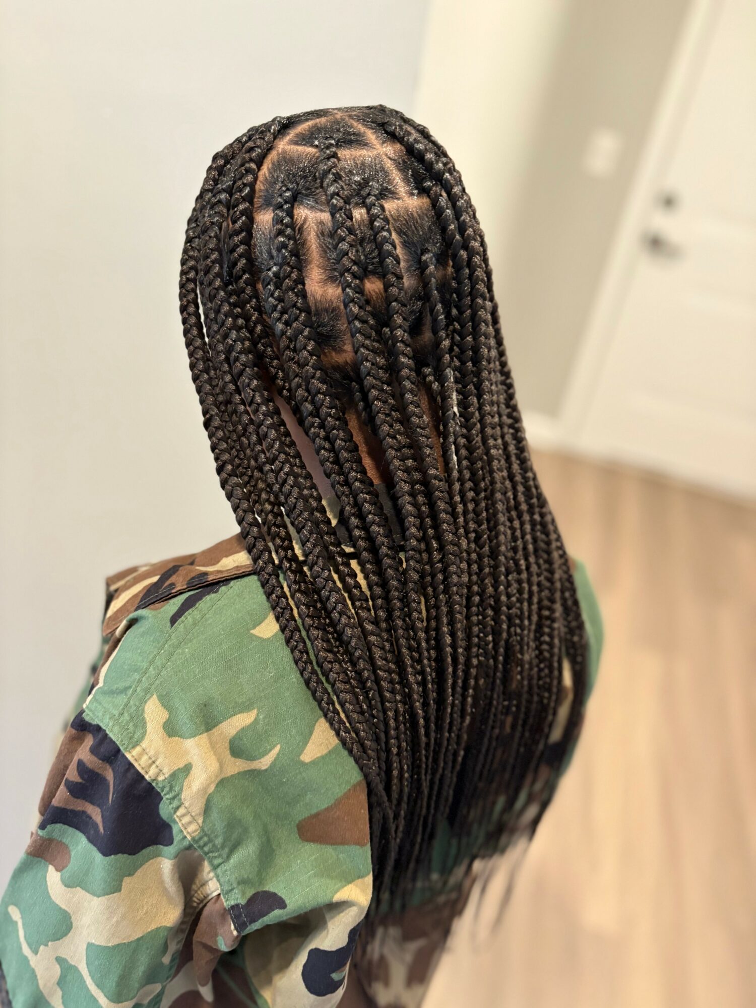 Person with long braided hair wearing a camouflage shirt, facing away from the camera, indoors.