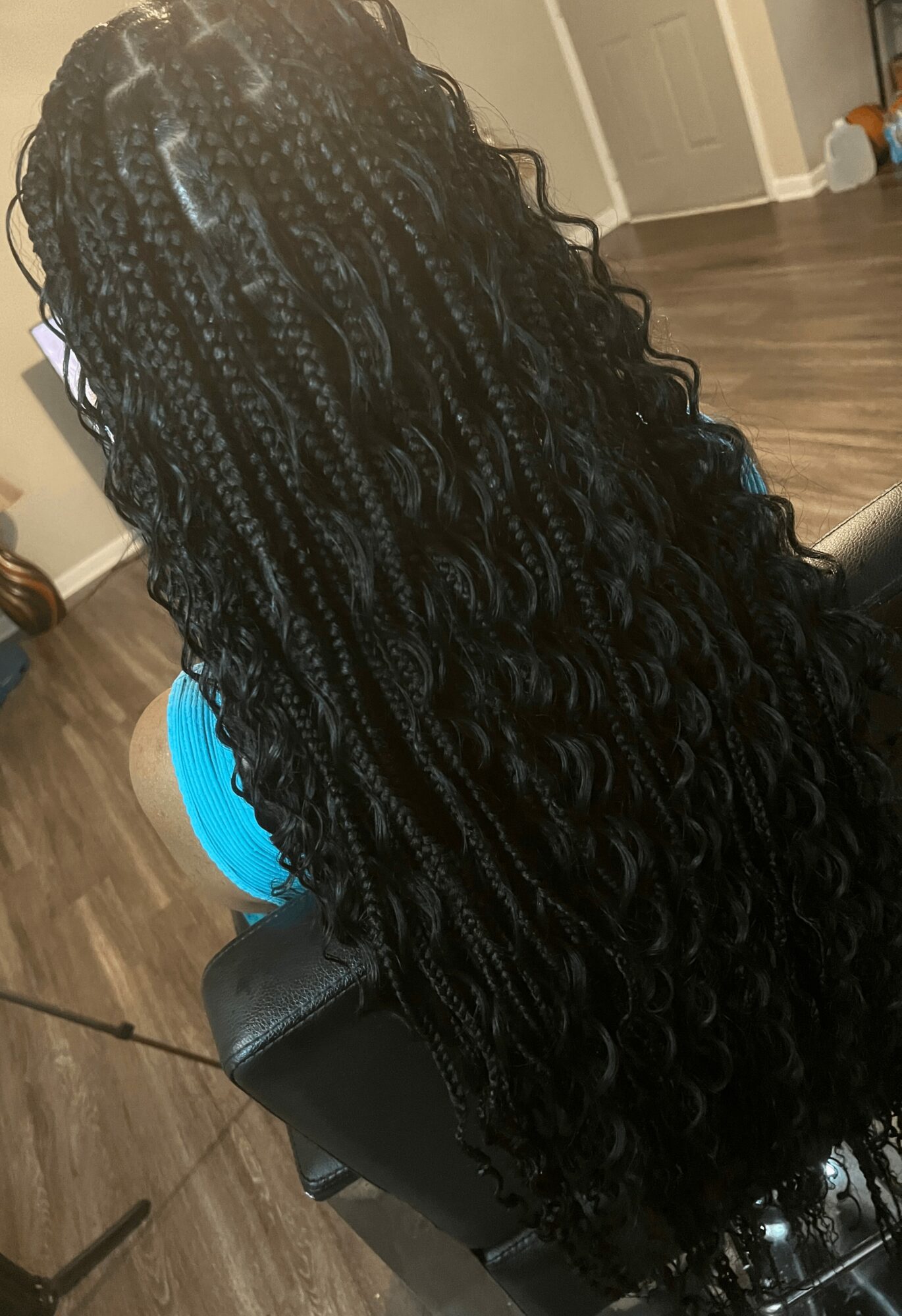 Person with long, curly, braided hair sitting in a room with wooden flooring and a door in the background.